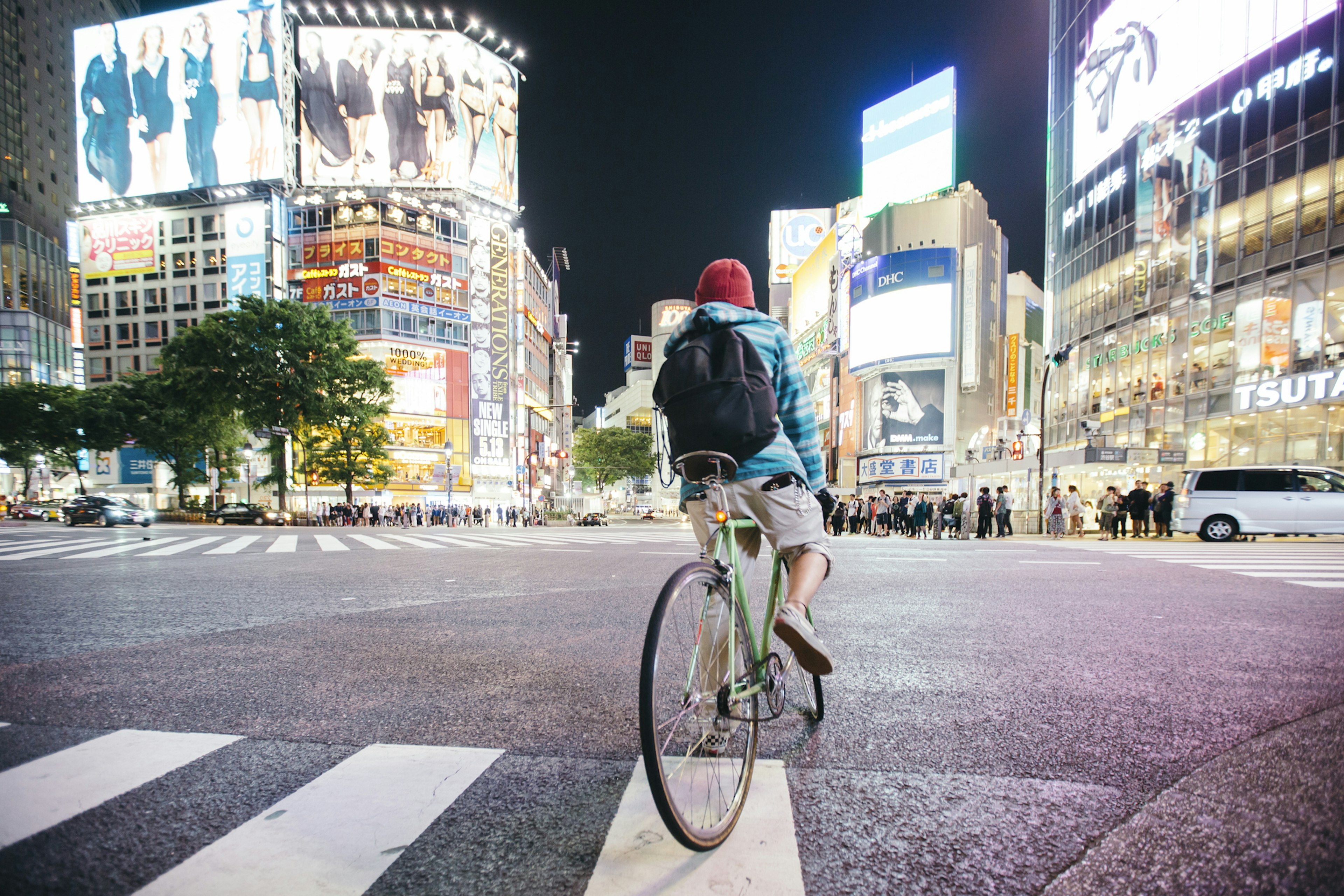 Young guy with backpack riding a bike at evening time on Shibuya crossing in Tokyo, Japan