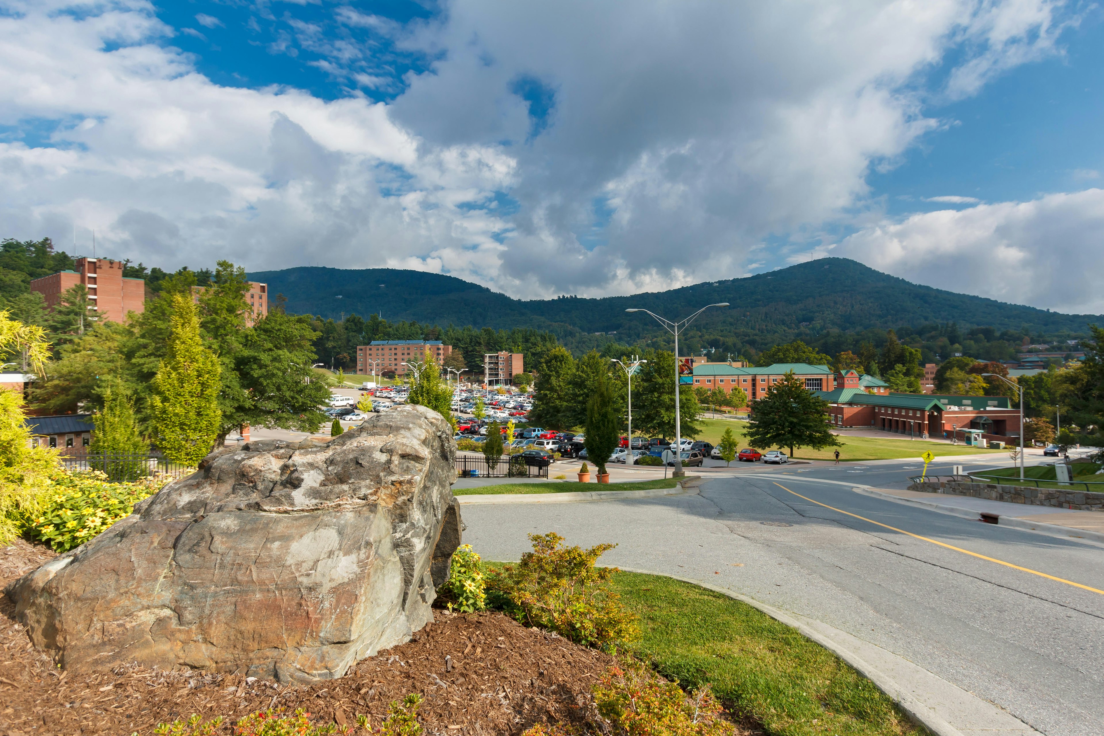 A university campus and parking lot surrounded by mountains under a cloudy sky