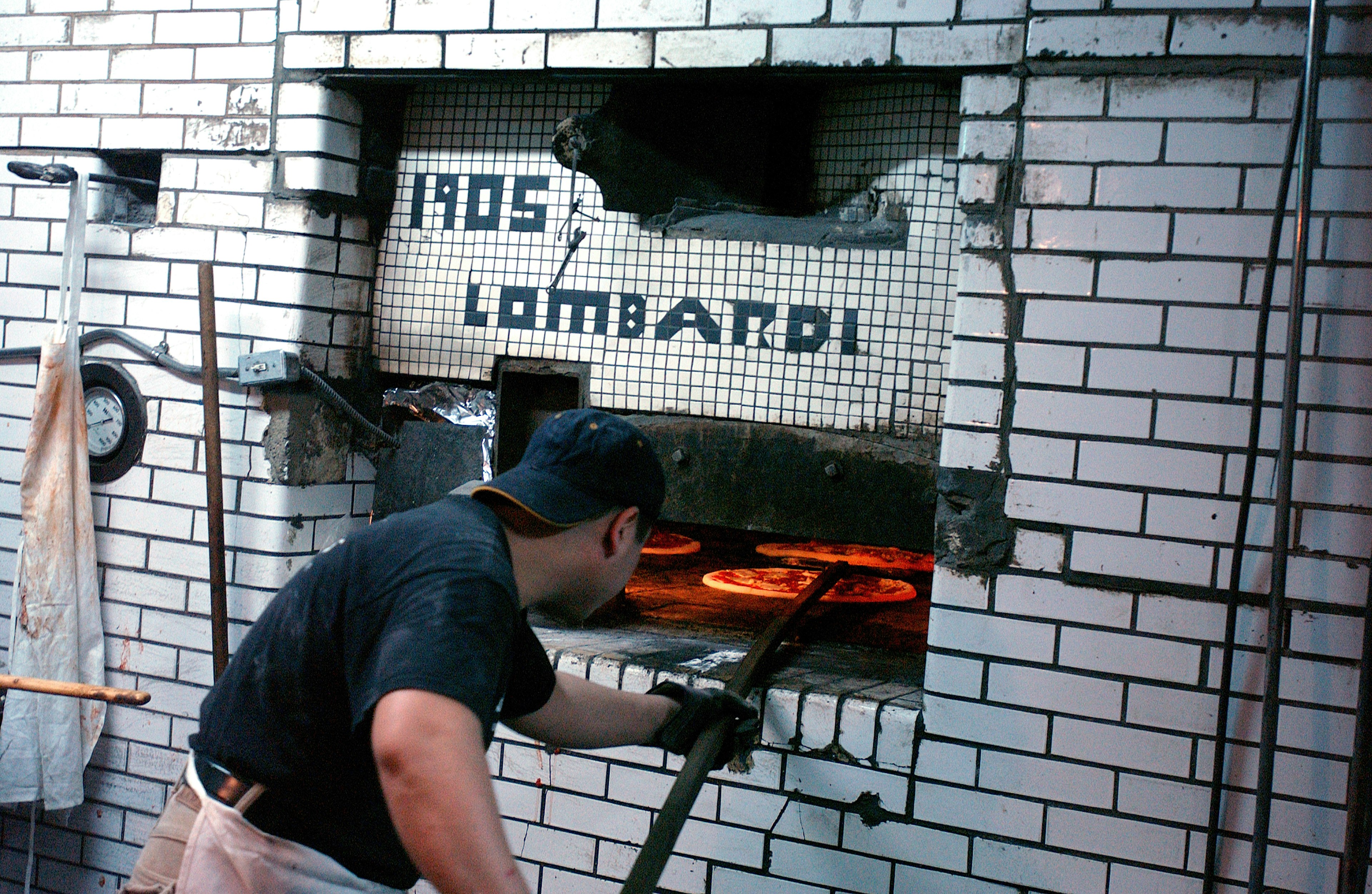 A pizza chef checking on the pizzas in the coal-fired oven at Lombardi's