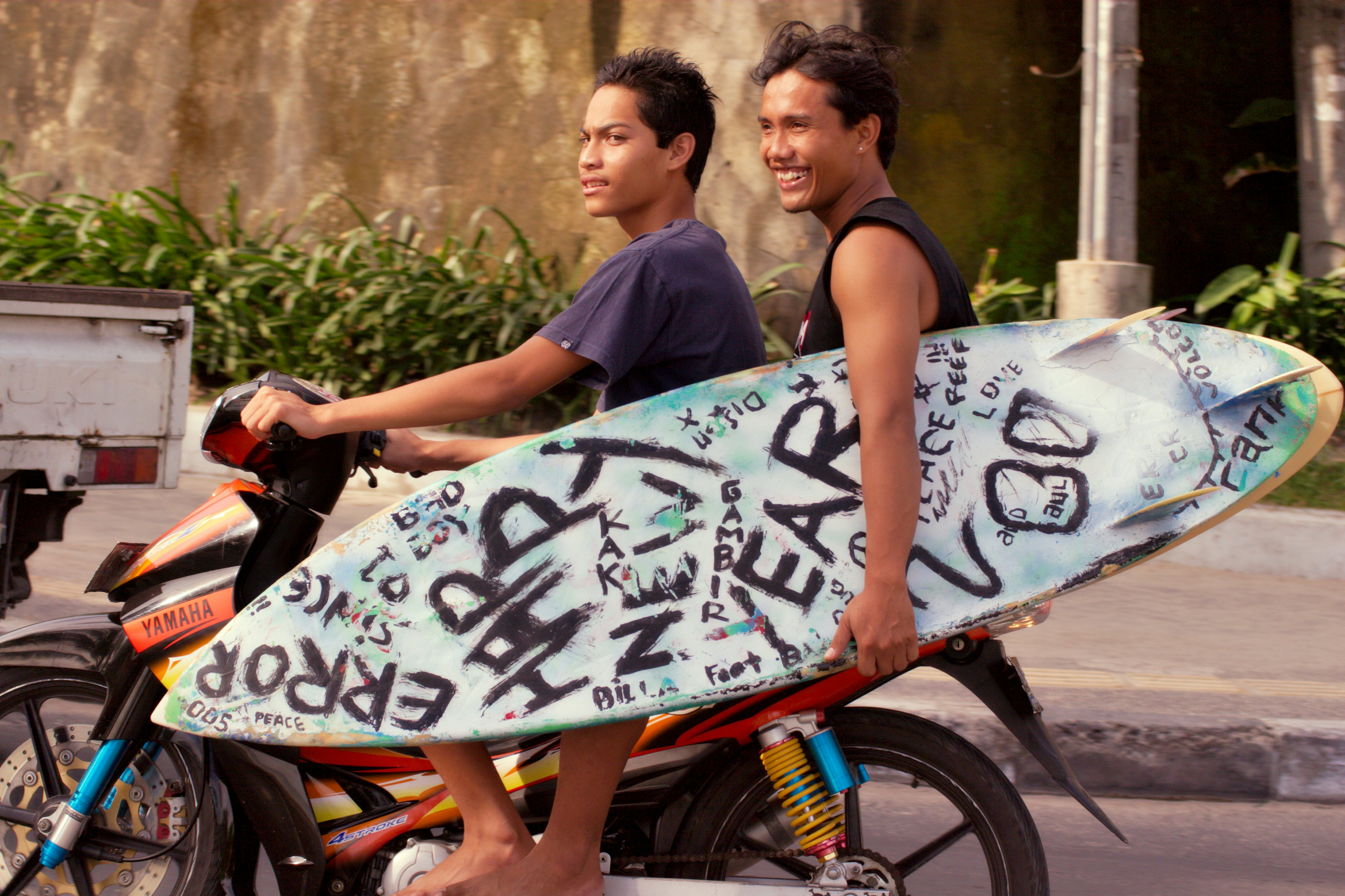 Two Balinese locals on a motor bike carrying a surfboard.