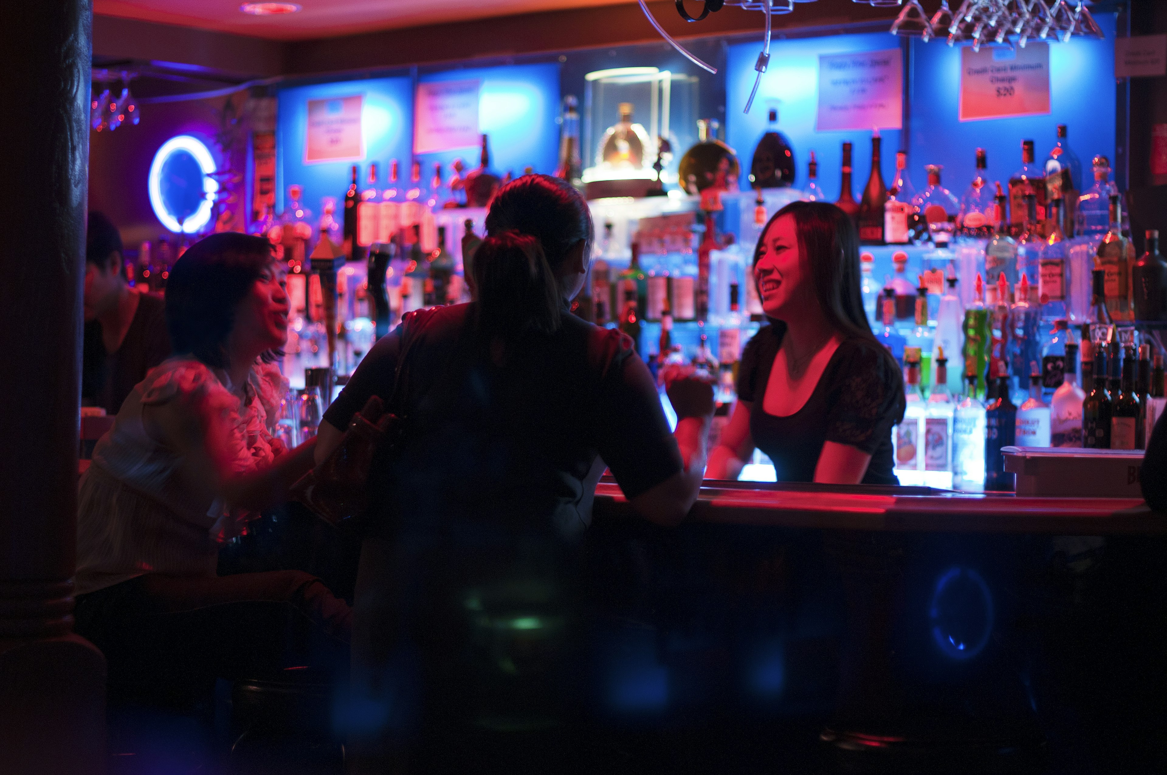 A bartender and patrons in a bar in San Francisco with moody pink-and-blue lighting