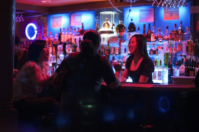 A bartender and patrons in a bar in San Francisco with moody pink-and-blue lighting