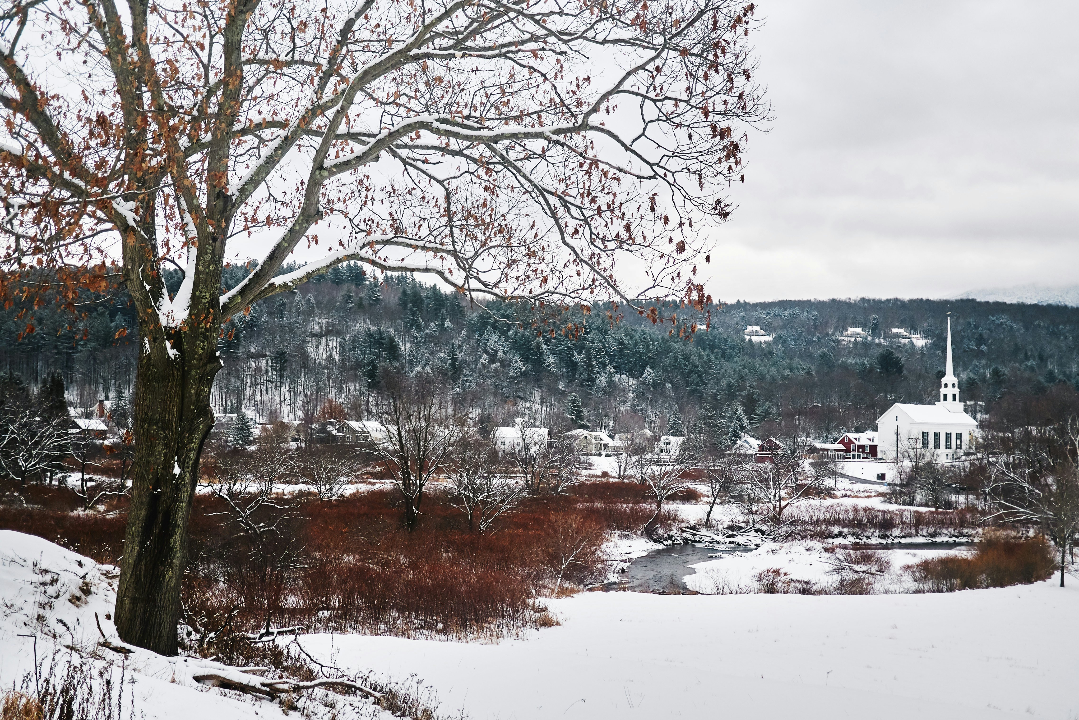 A snow-covered Vermont ski town with a church steeple overlooking a pond.