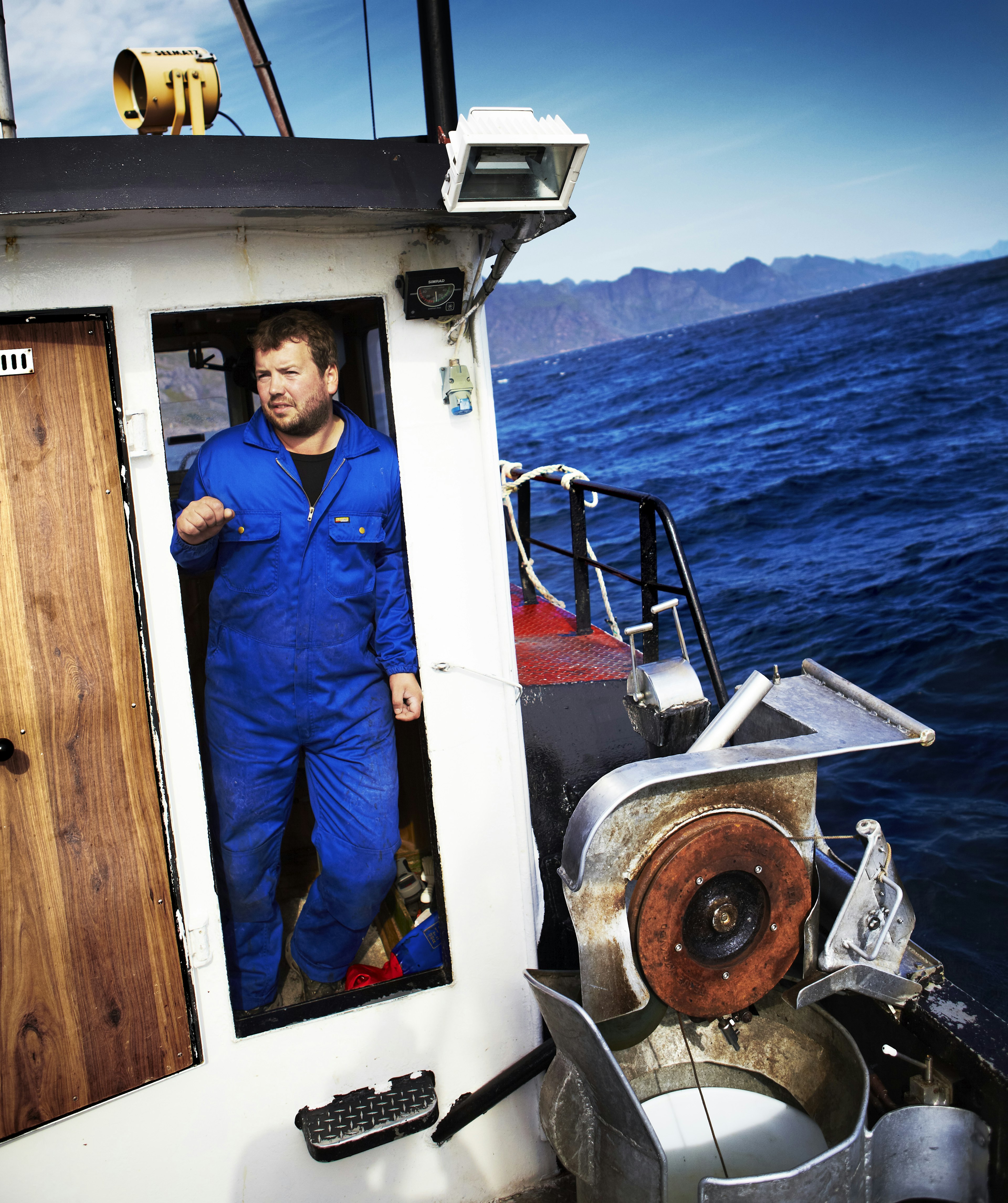 A fisherman in blue jumpsuit, with blue waters beyond