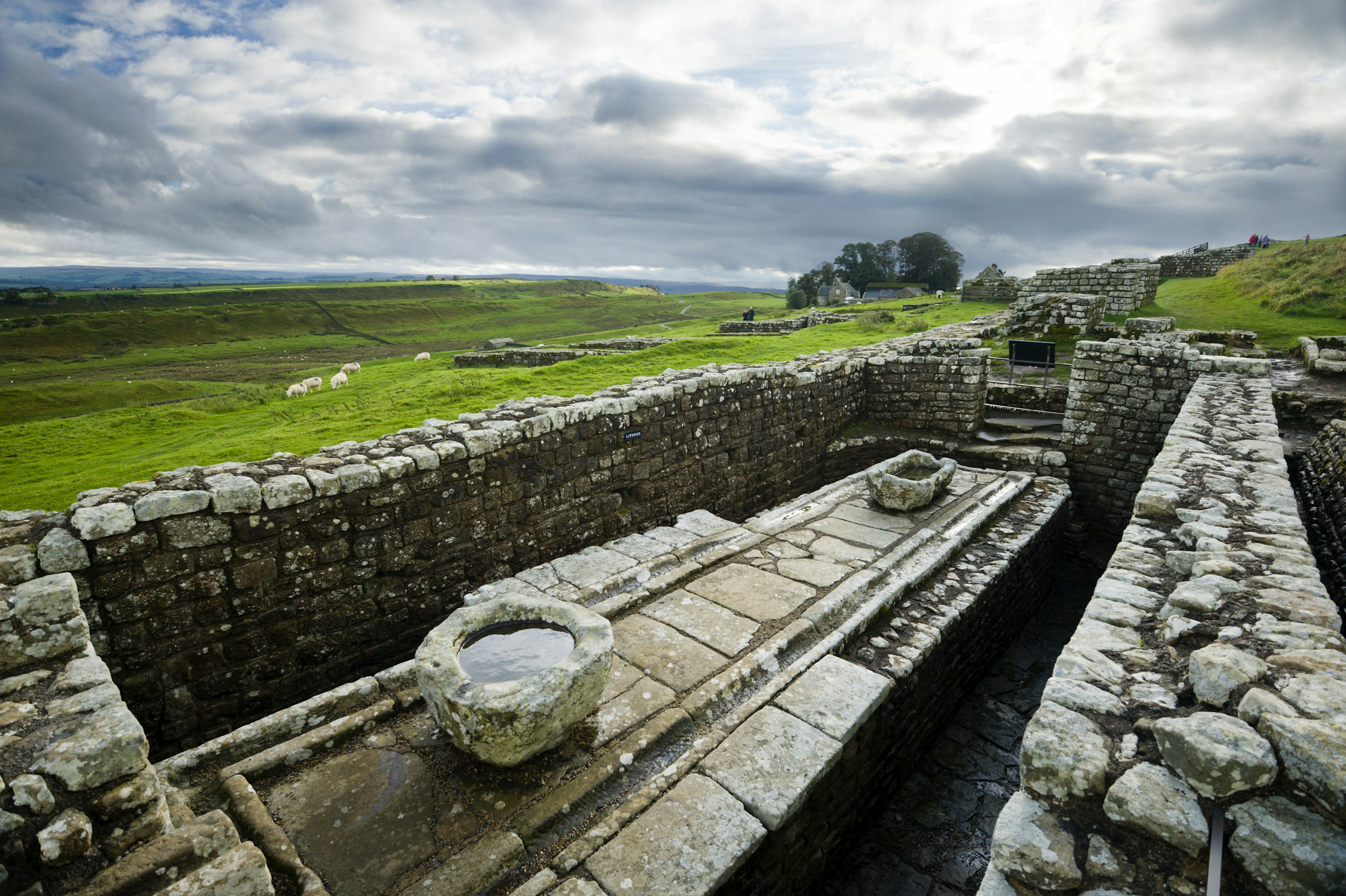 Latrines at Hadrian's Wall with cloudy skies and green moors in the background.