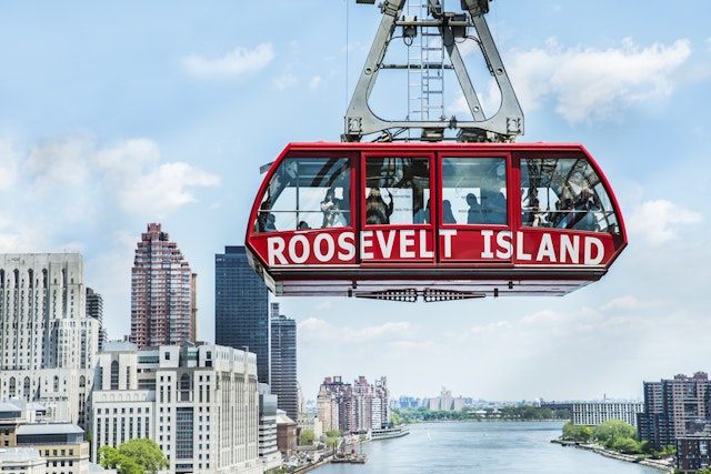 The bright-red Roosevelt Island tram suspended over the East River, with Manhattan skyscrapers gleaming in the distance