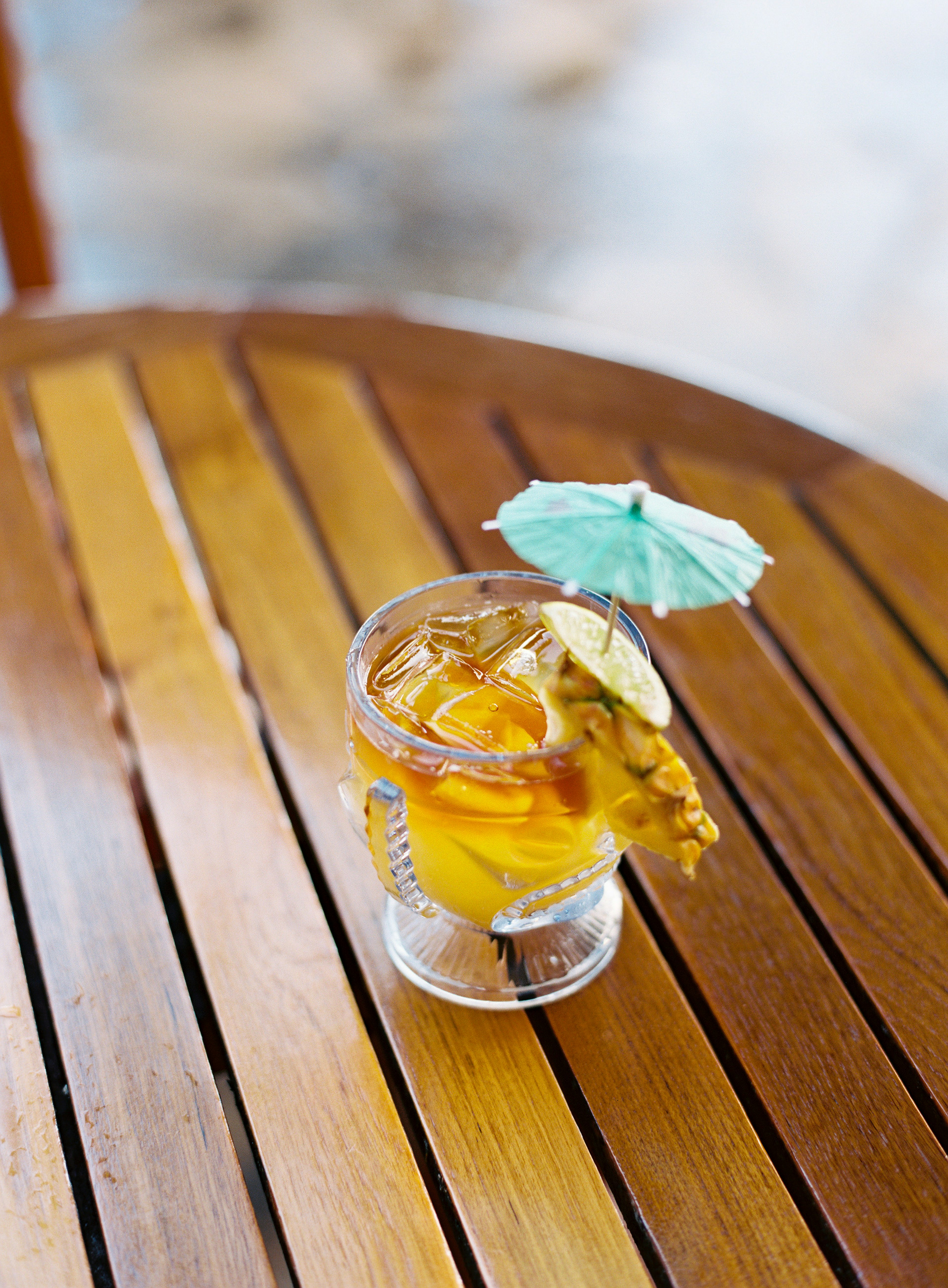 A Mai Tai cocktail with a little umbrella sits on a wooden table