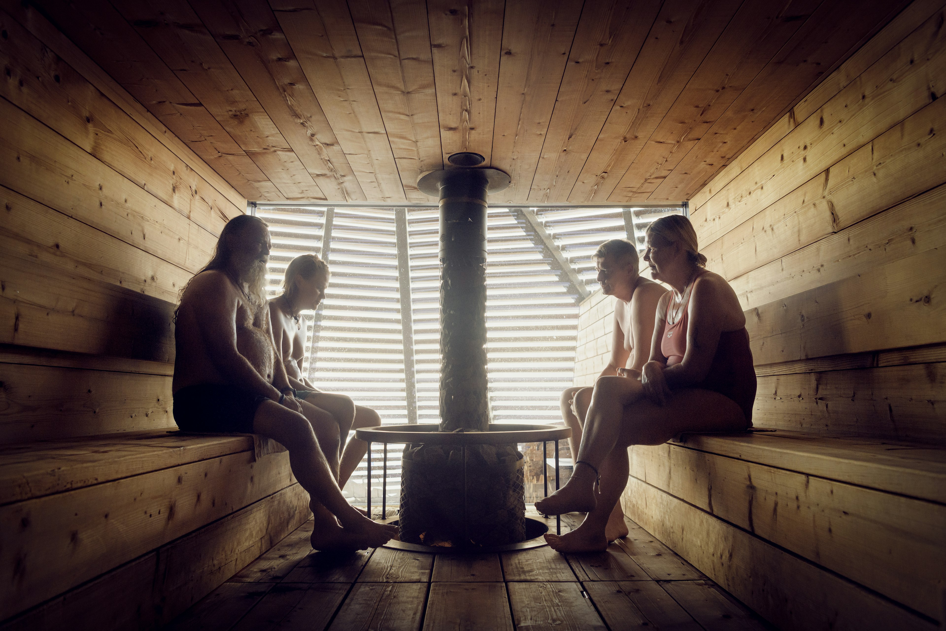 Four people are silhouetted in a wooden sauna room with a central stove in Helsinki, Finland