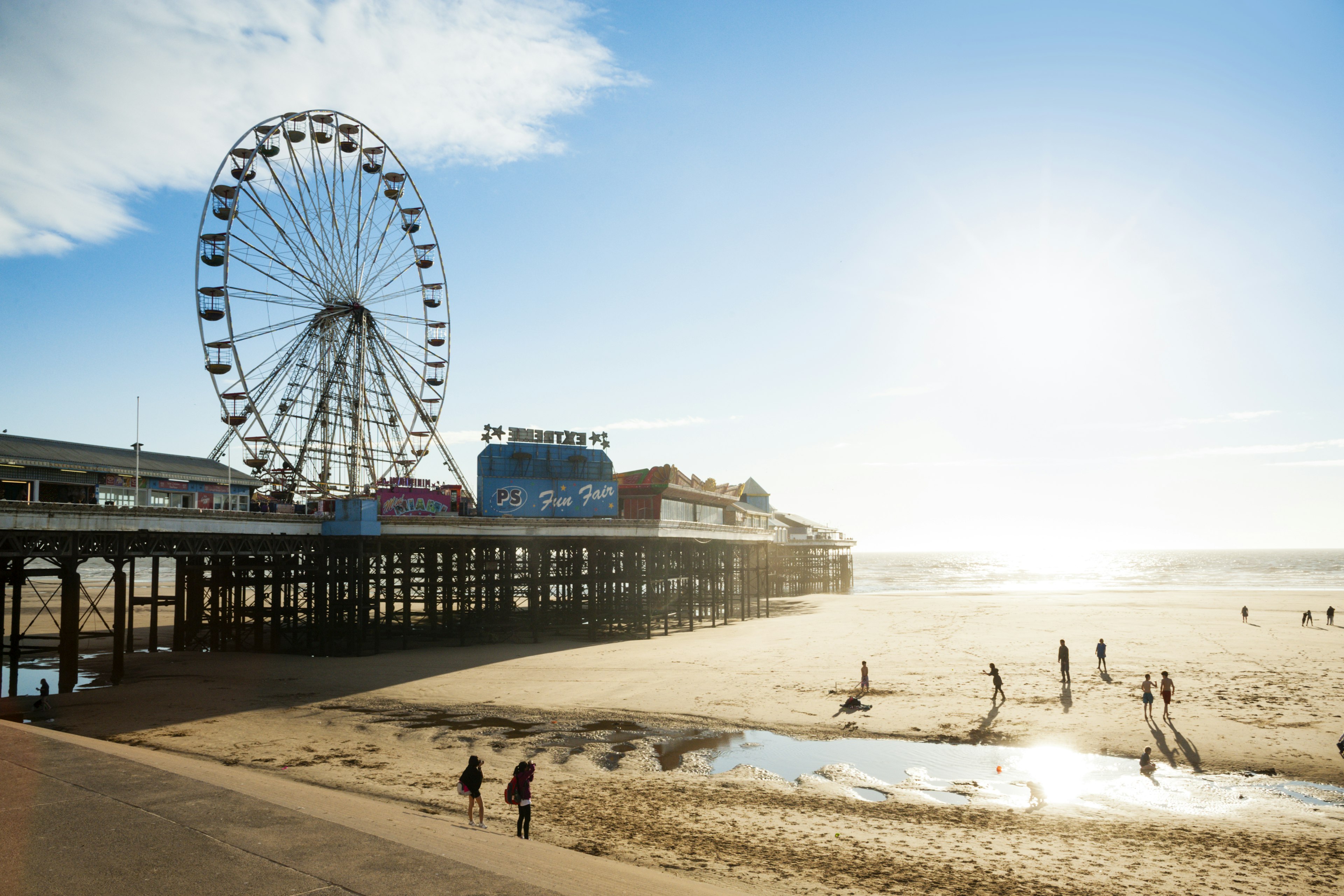 A Ferris wheel on a pier next to a broad sandy beach in the sunshine