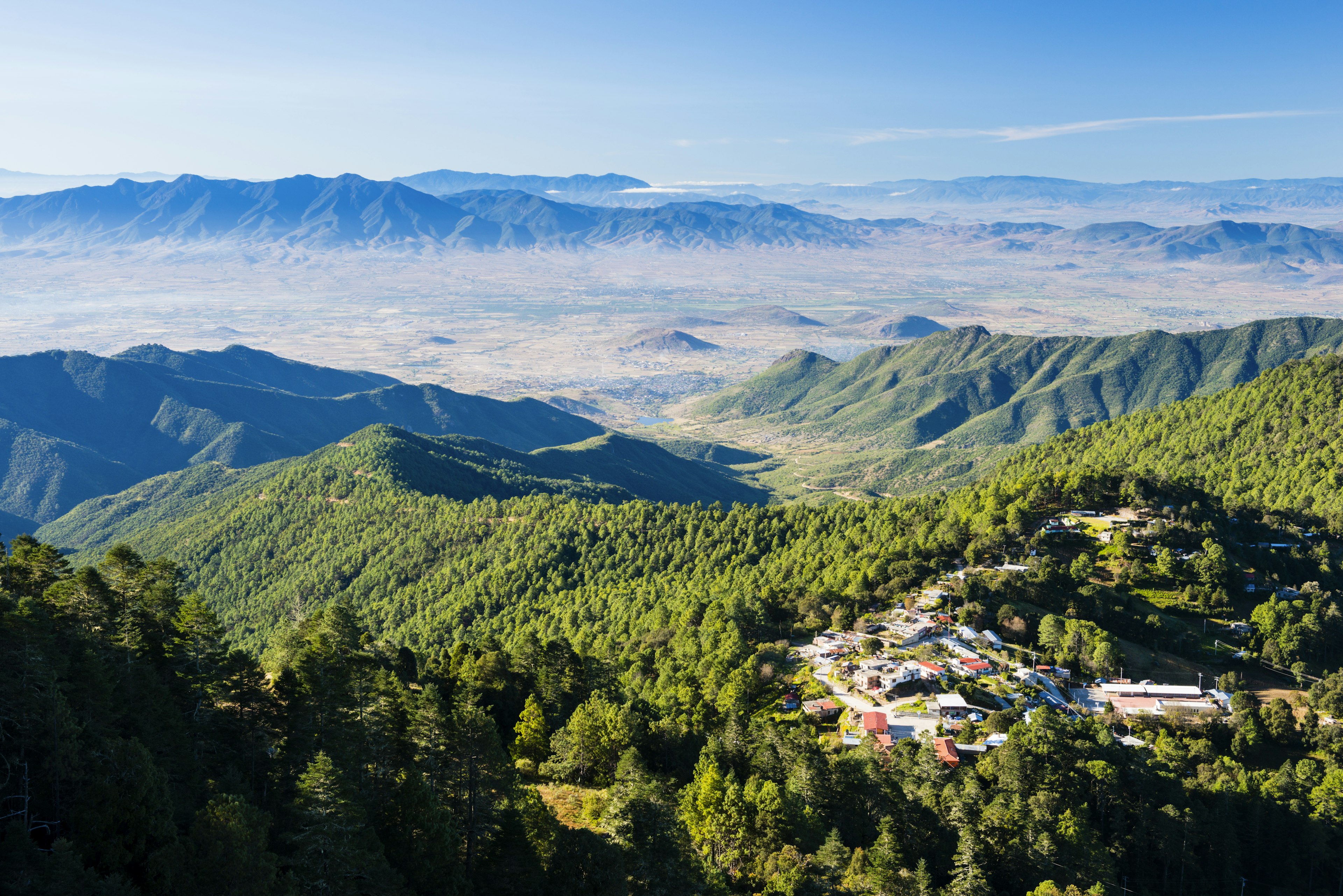 An aerial shot of the mountain villages of the Pueblos Mancomunados, with green slopes and cloudy valleys