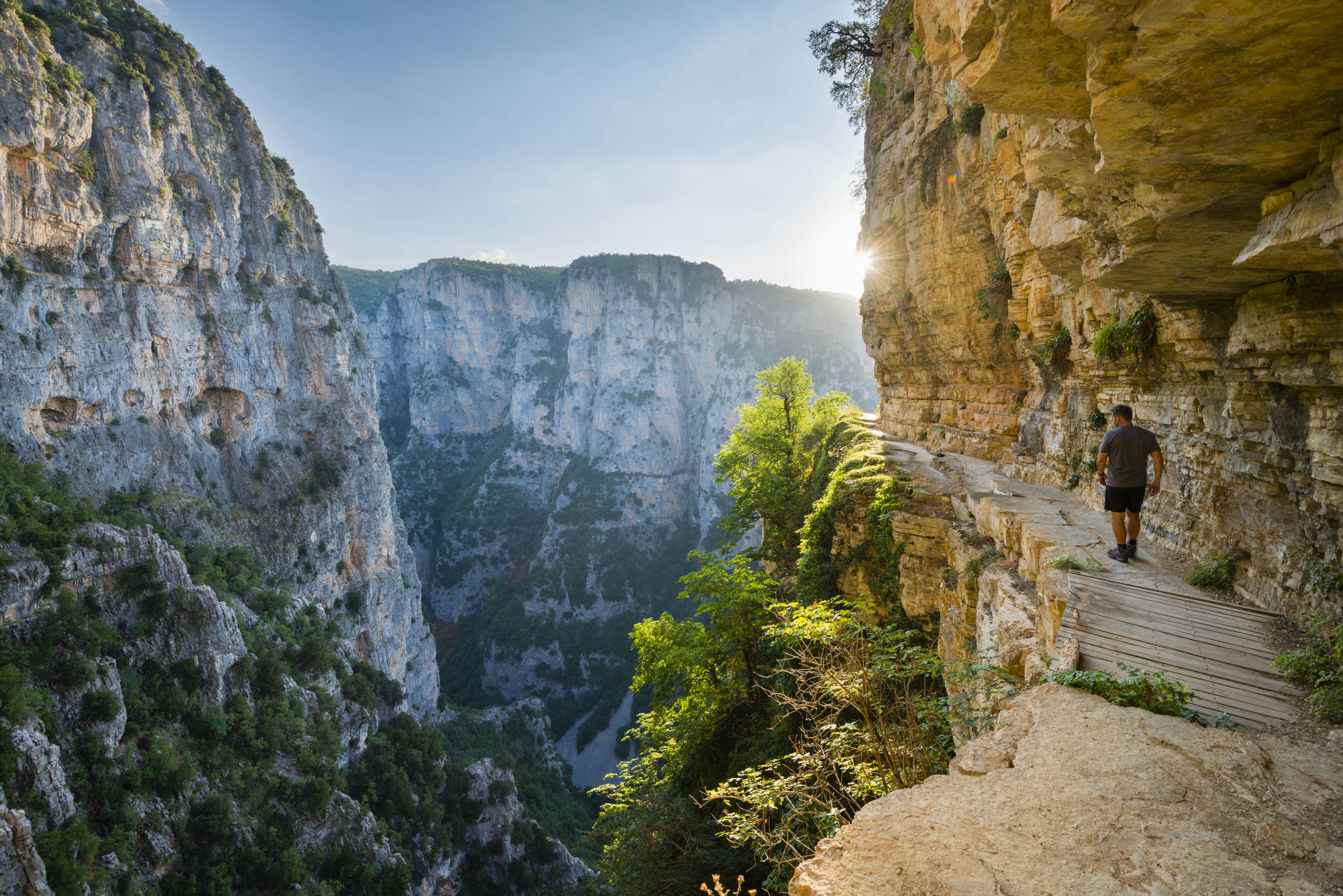 A man follows a path carved into the side of a cliffside, which plunges off to his left into the gorge below