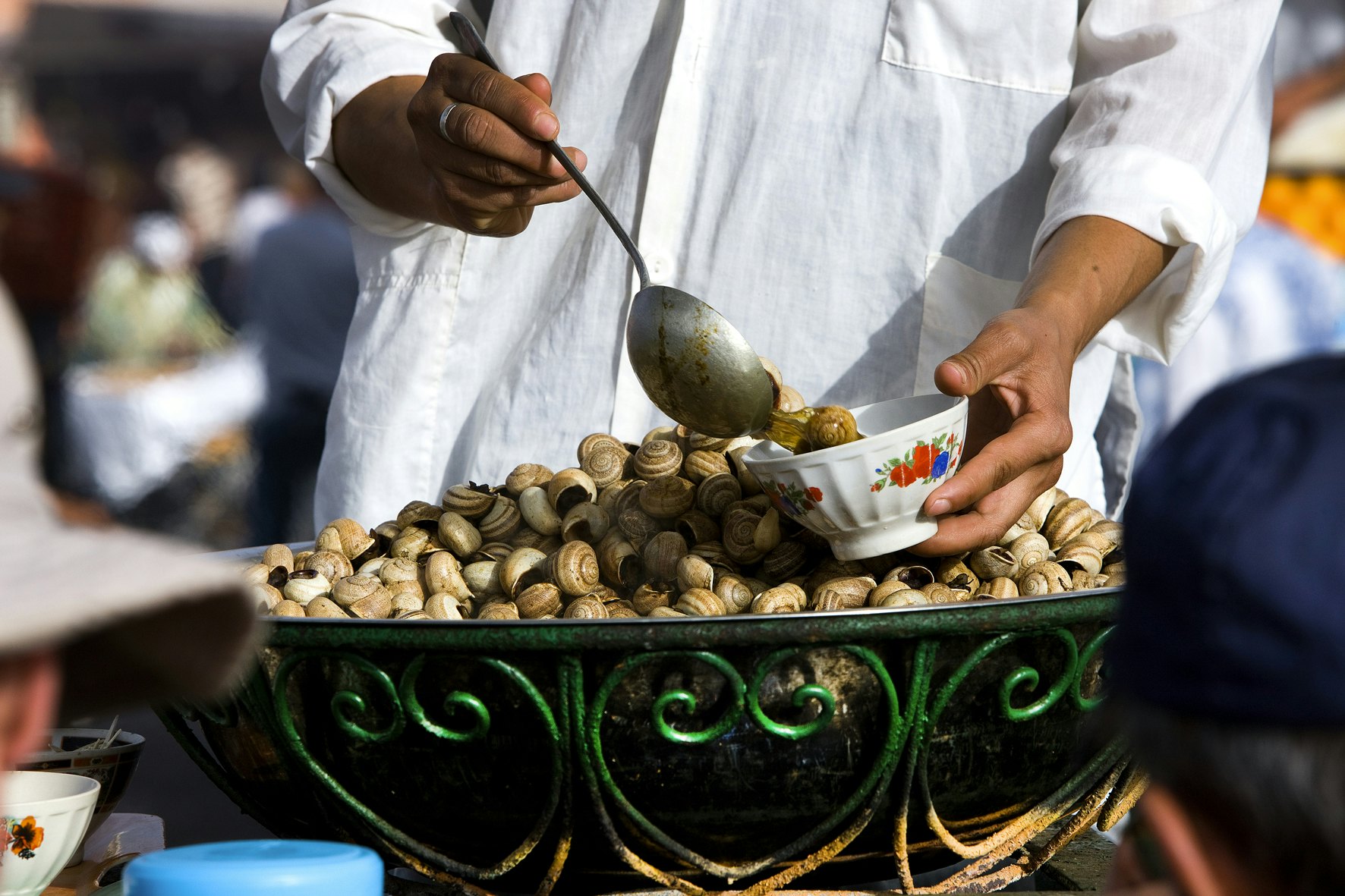 A man serves cooked snails in a bowl in a Marrakesh market.