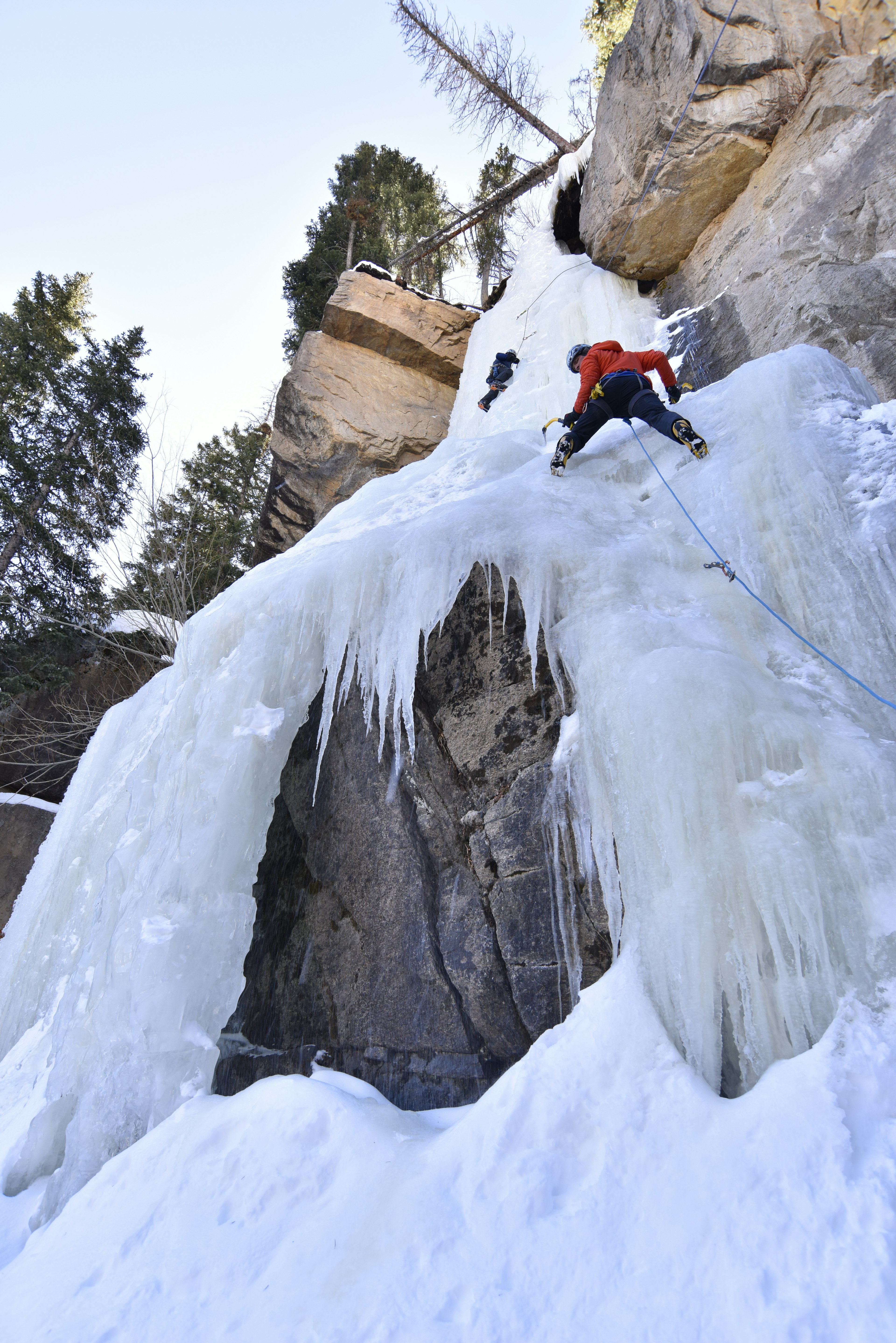 A pair of people climb up a large icy structure in Estes Park, Colorado.