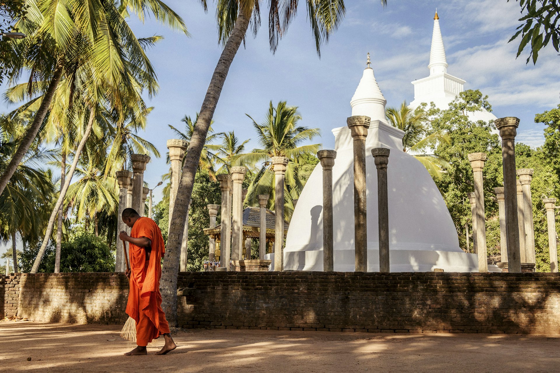 An orange-robed monk sweeps the ground at a temple in Mihintale in Sri Lanka