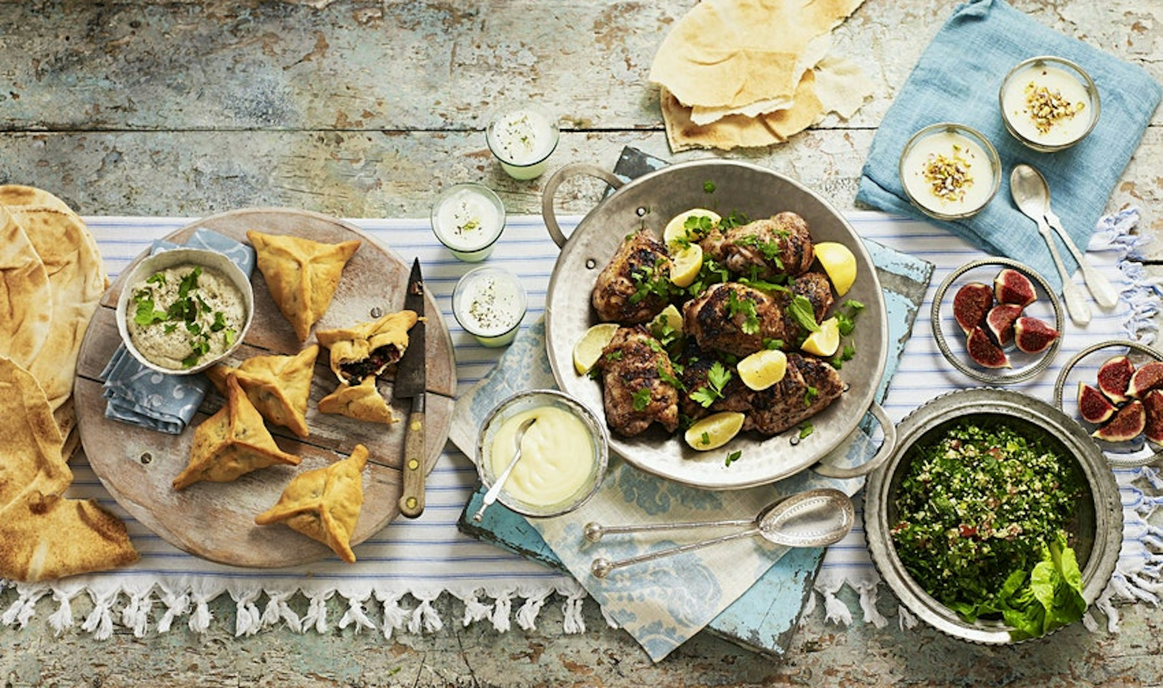 A platter of Lebanese food with dips, hummus, chicken, dates and greens