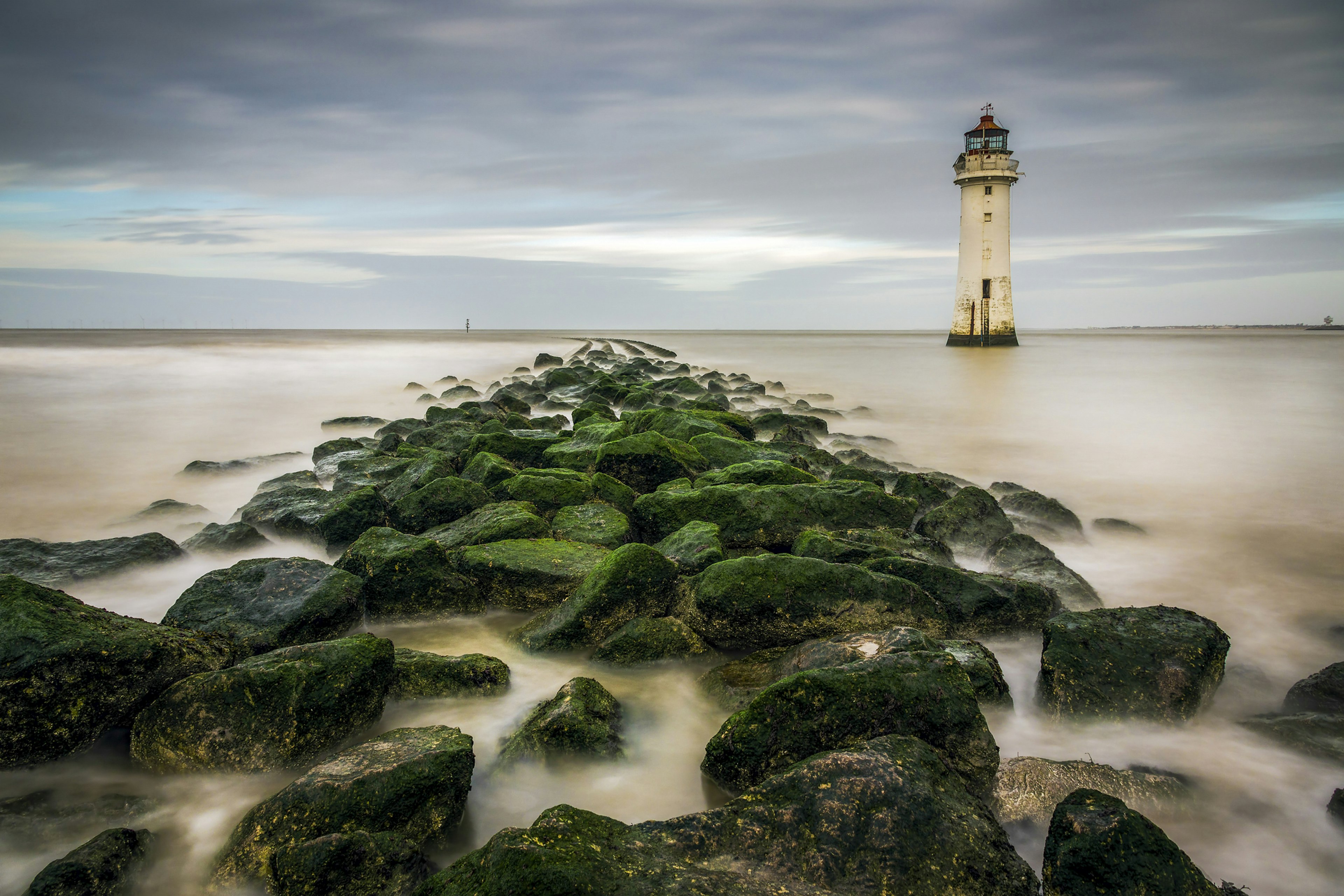 View of New Brighton Lighthouse with mossy rocks on the beach in the foreground