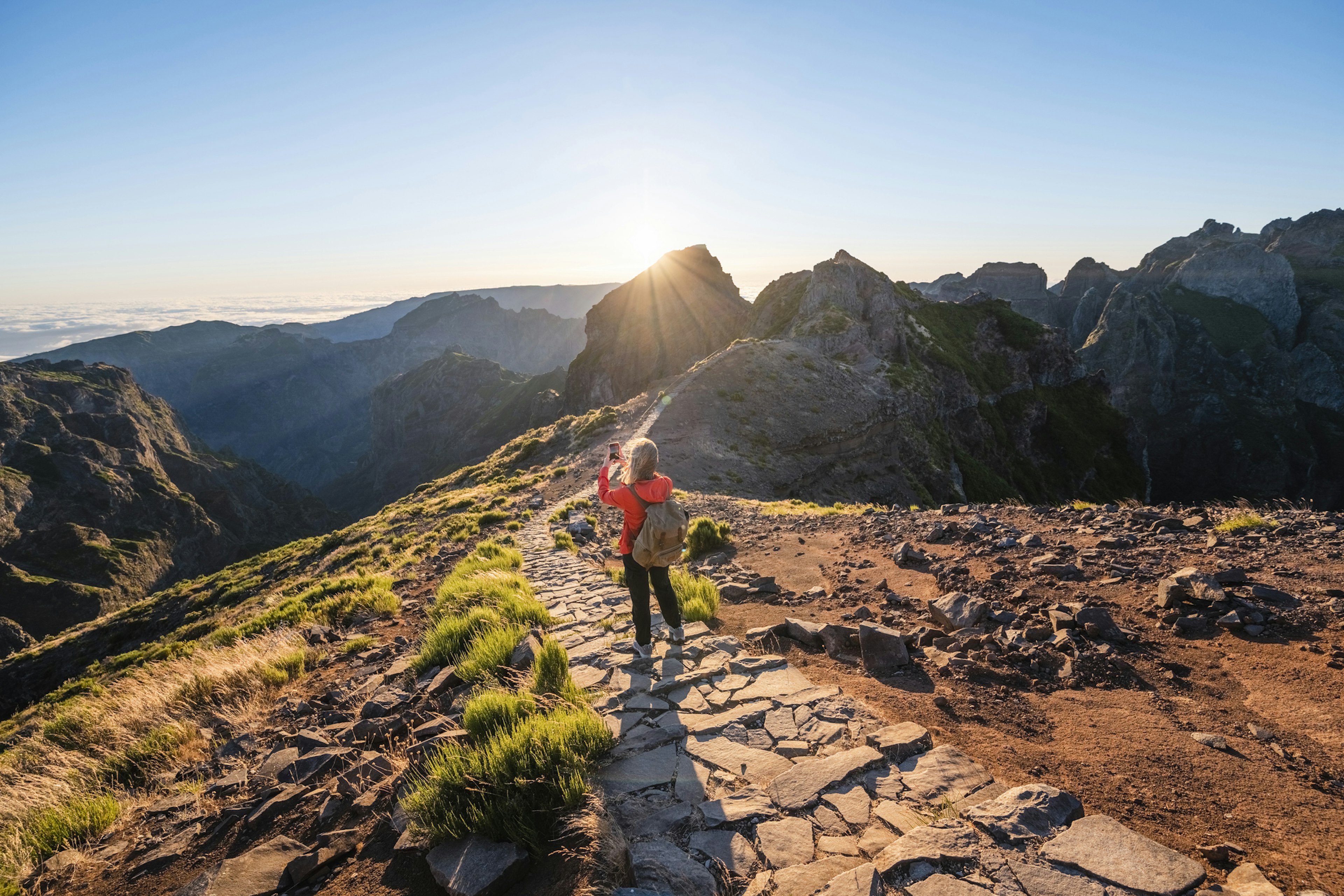 Woman tourist photographing with smartphone at Pico do Arieiro at sunset, Madeira Island, Portugal.