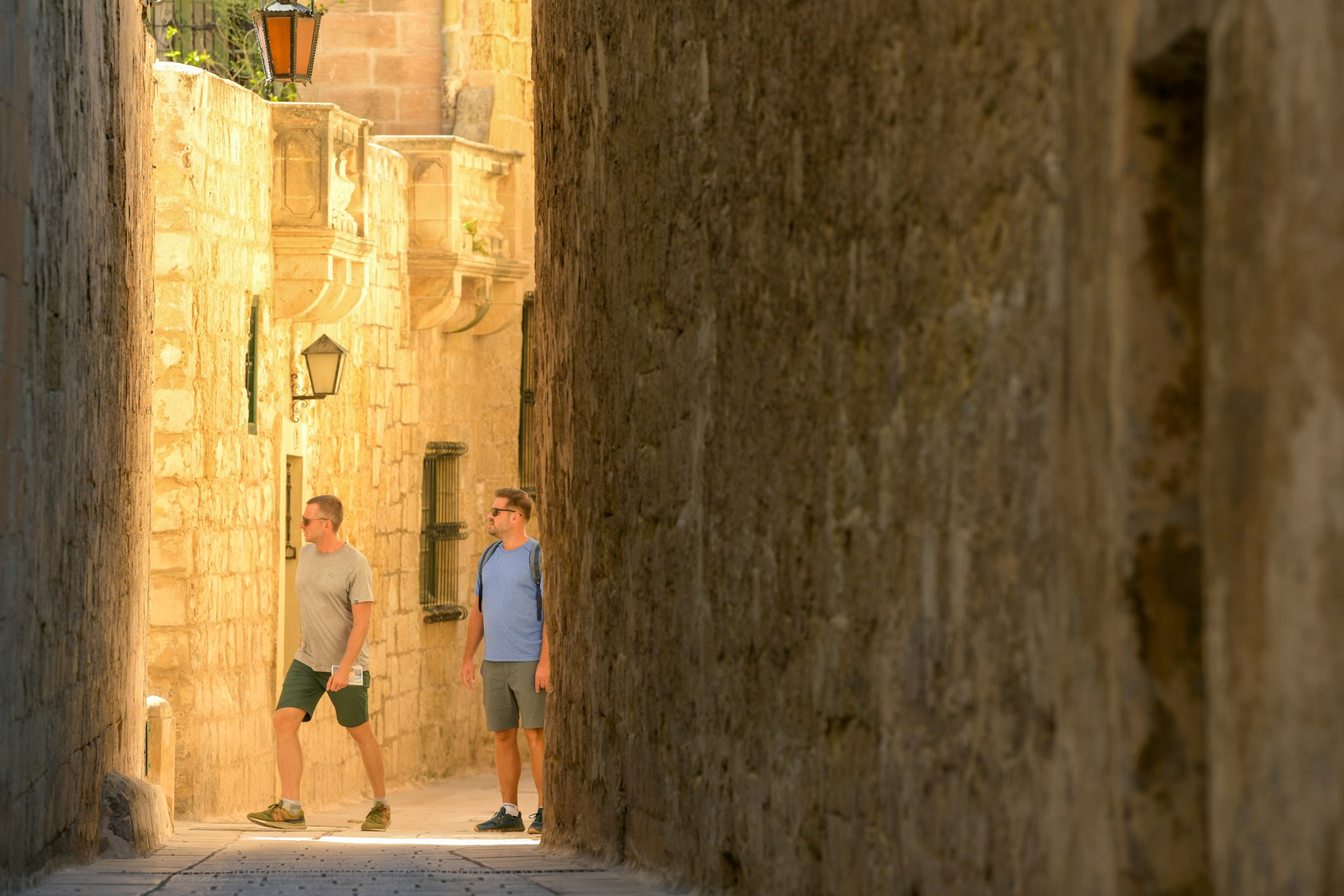 Two men walk in an alley partly cast in shadow in Mdina, Malta