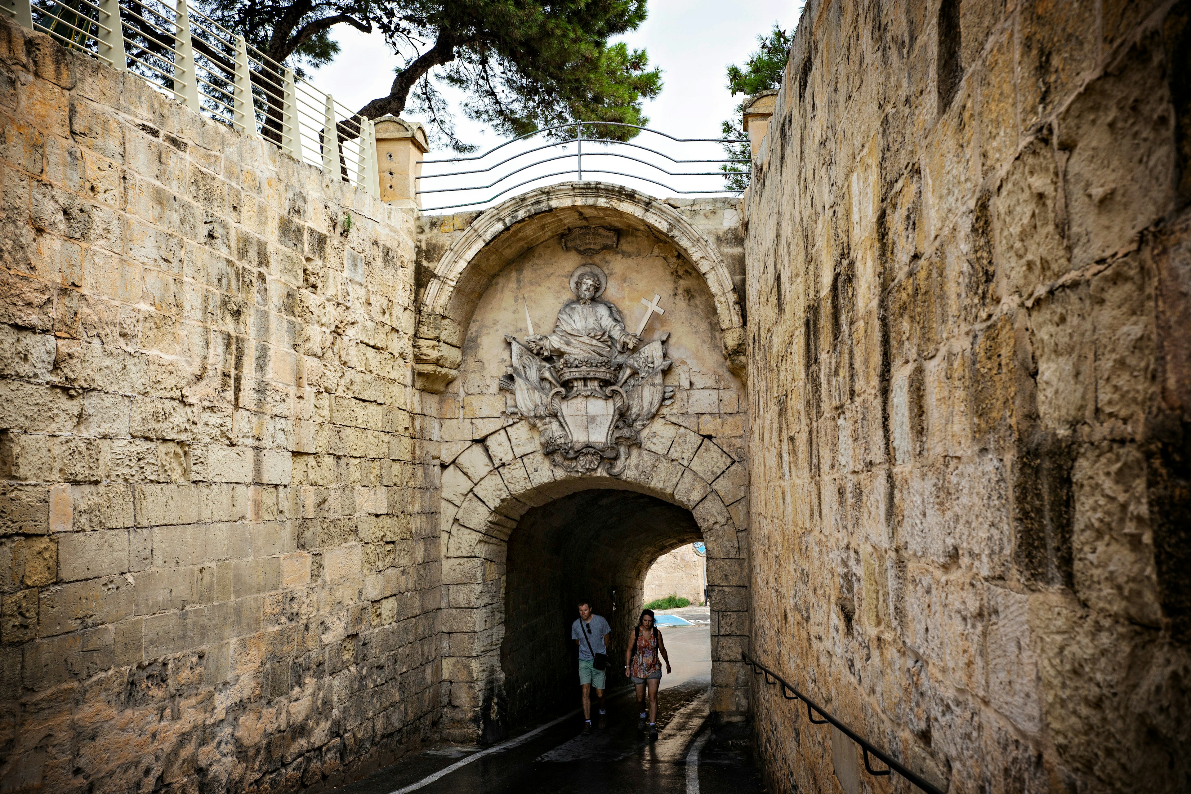 Two people walk through a massive stone portal, an entrance to the ancient town of Mdina, Malta