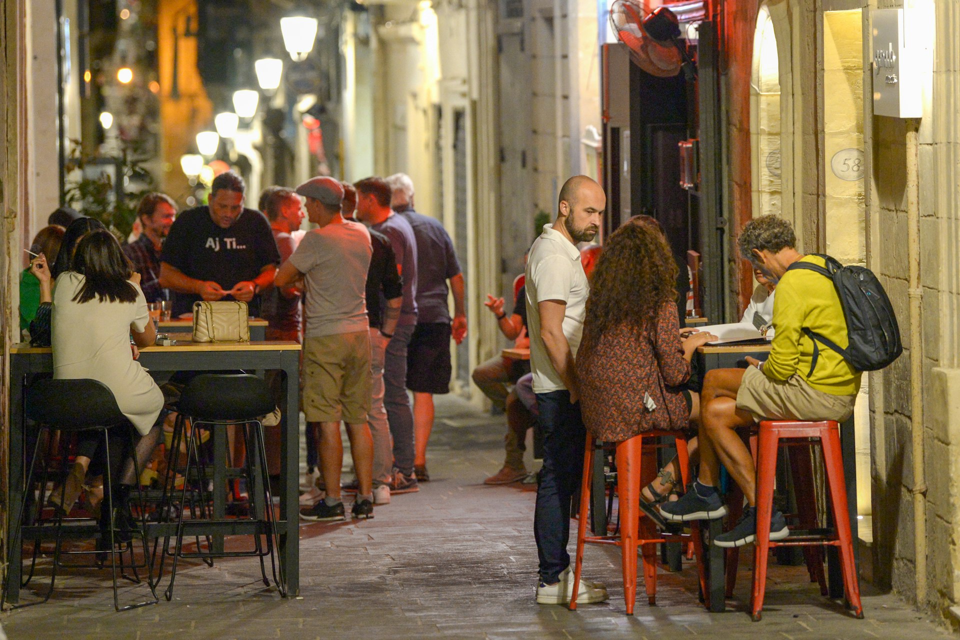 People sit at tables in a bar on a narrow street in Valletta, Malta