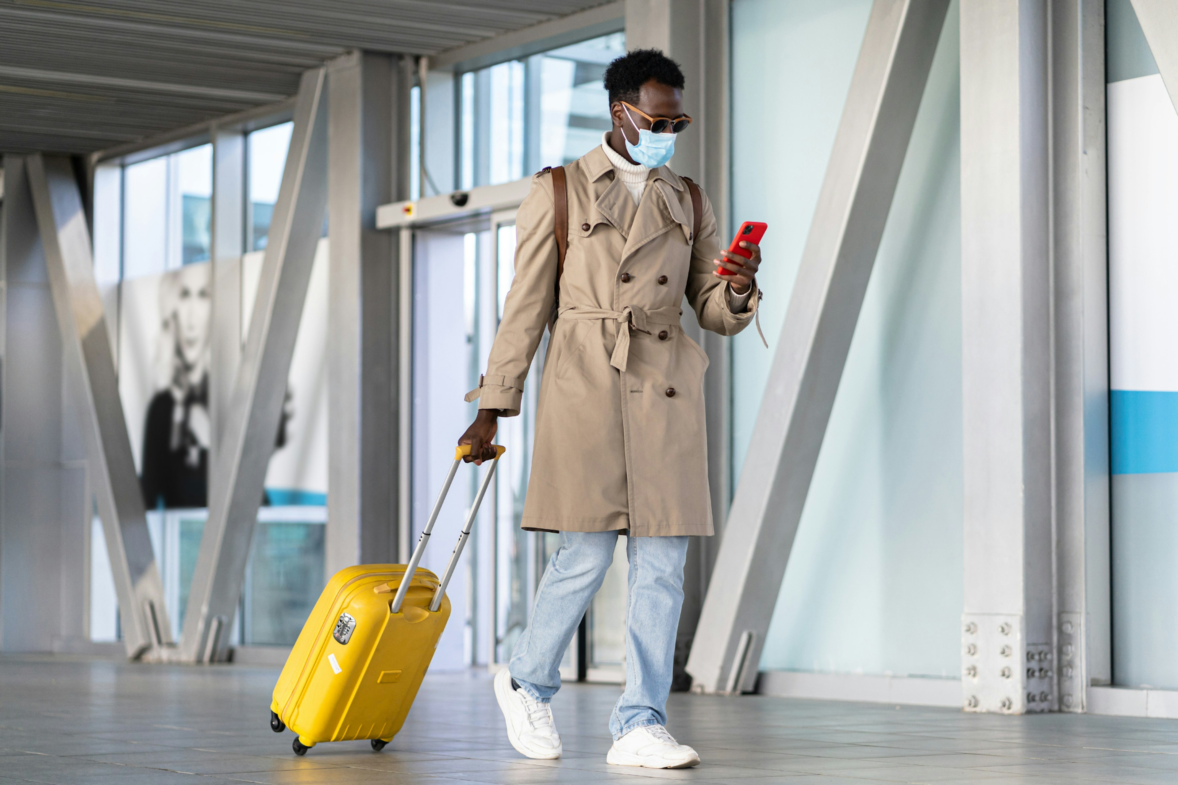 Man walking into airport with suitcase and wearing a face mask