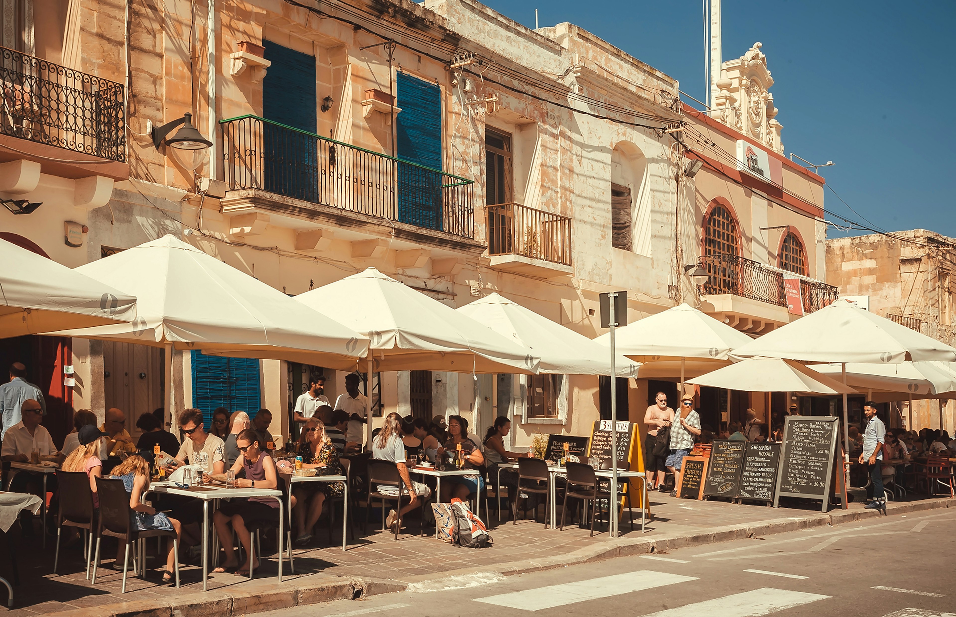 Crowd of people sitting at local restaurants, waiting for food on sunny and historical city street