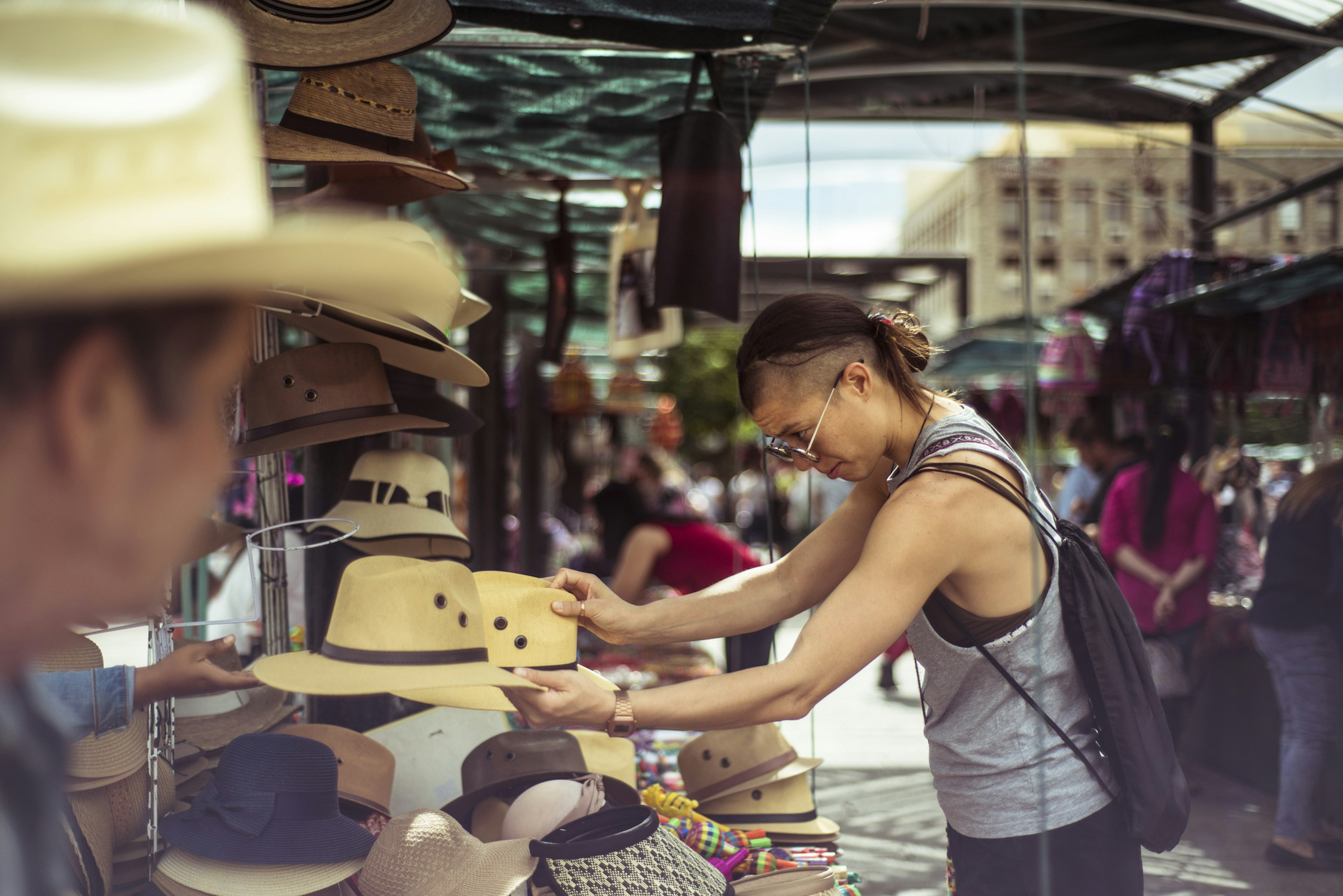 A person wearing a vest and sunglasses looks over a display of cowboy hats at an open-air market in Guadalajara