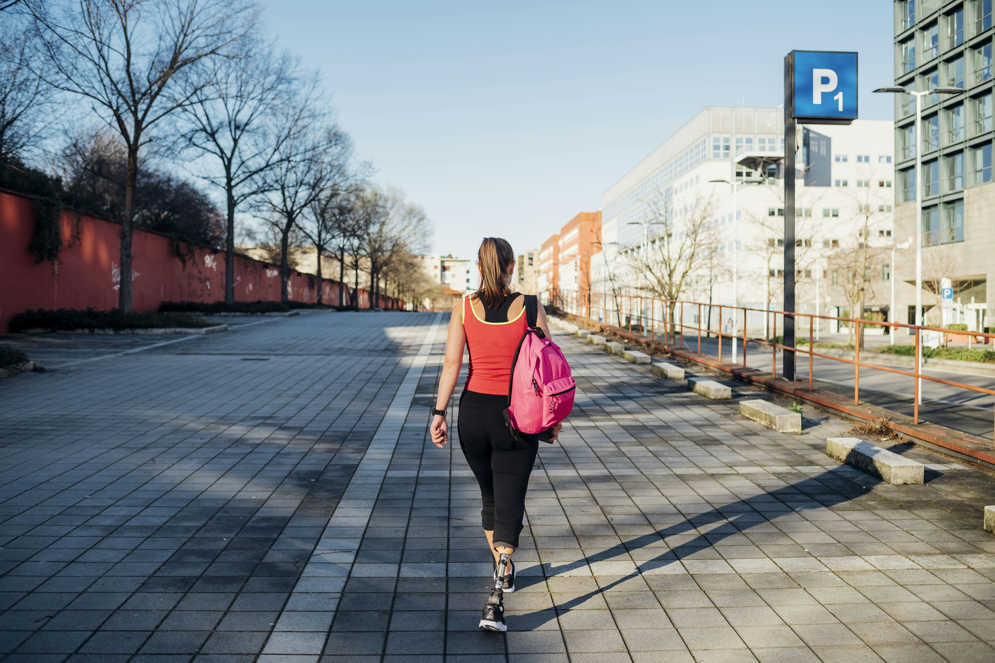 Sporty young woman with leg prosthesis walking on car park in the city