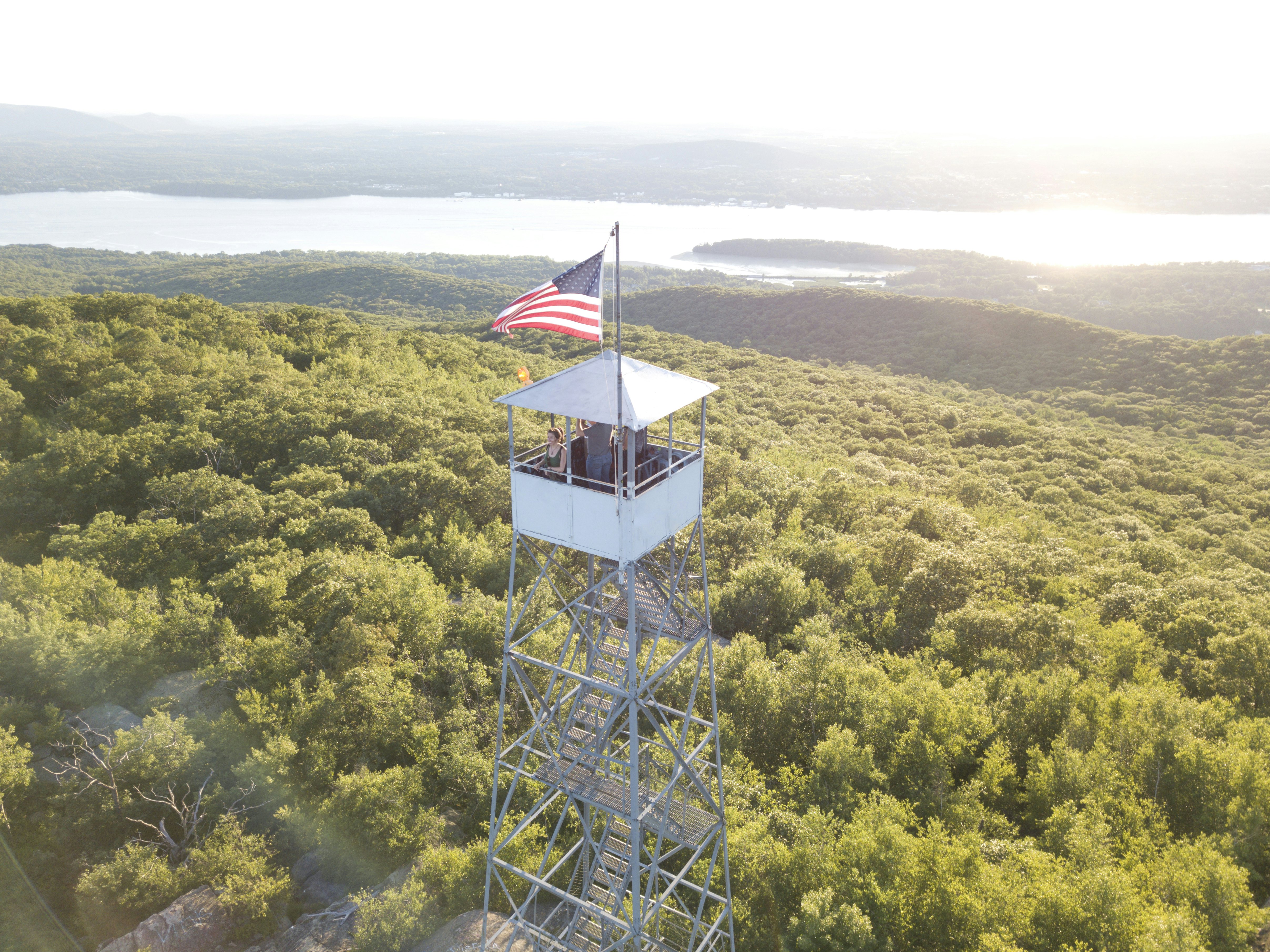 A woman in a tower with an American flag, looking out over the Hudson River, greenery and mountains