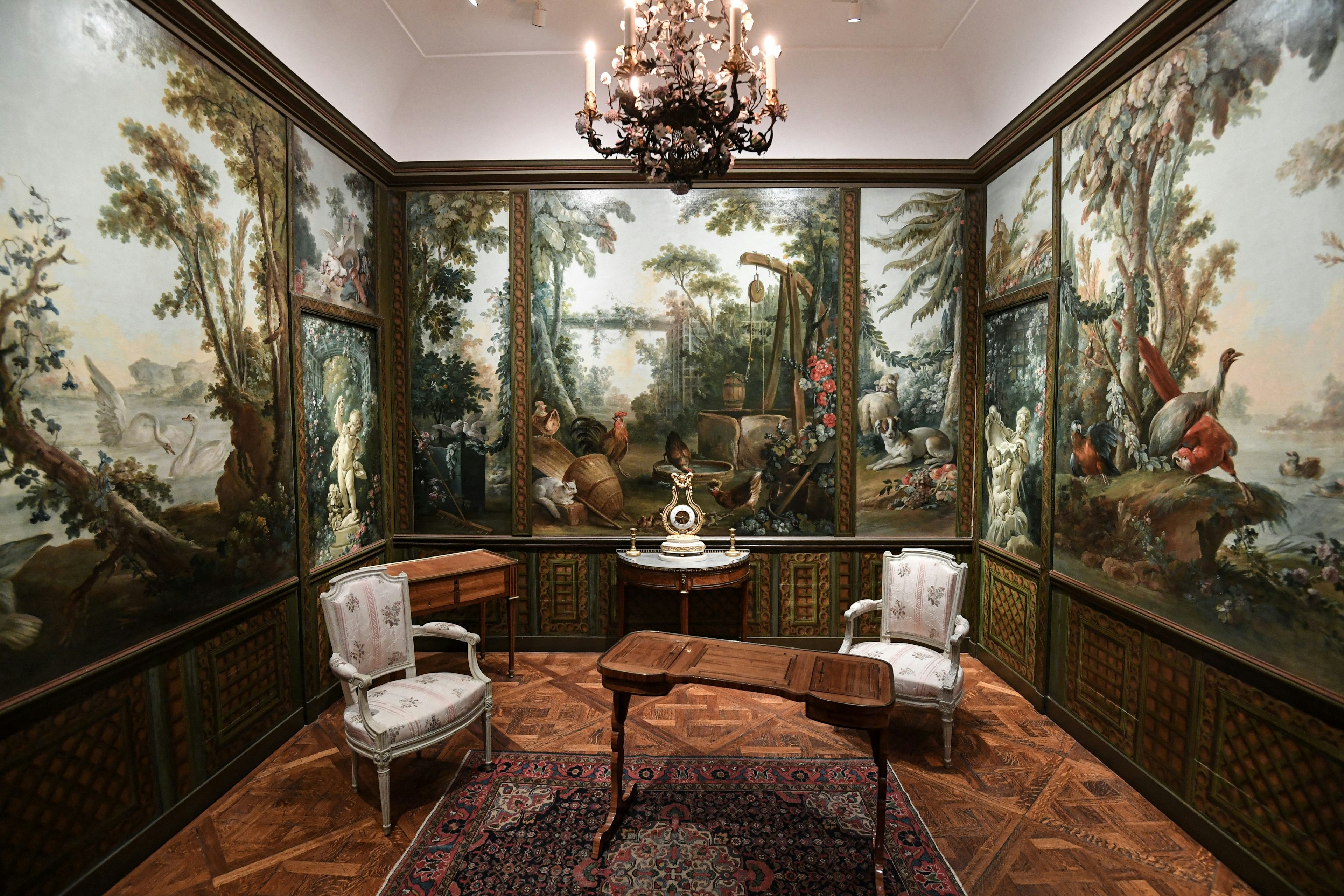 A room with walls painted with murals of woodland and birds, with an ornate table and two chairs in the center