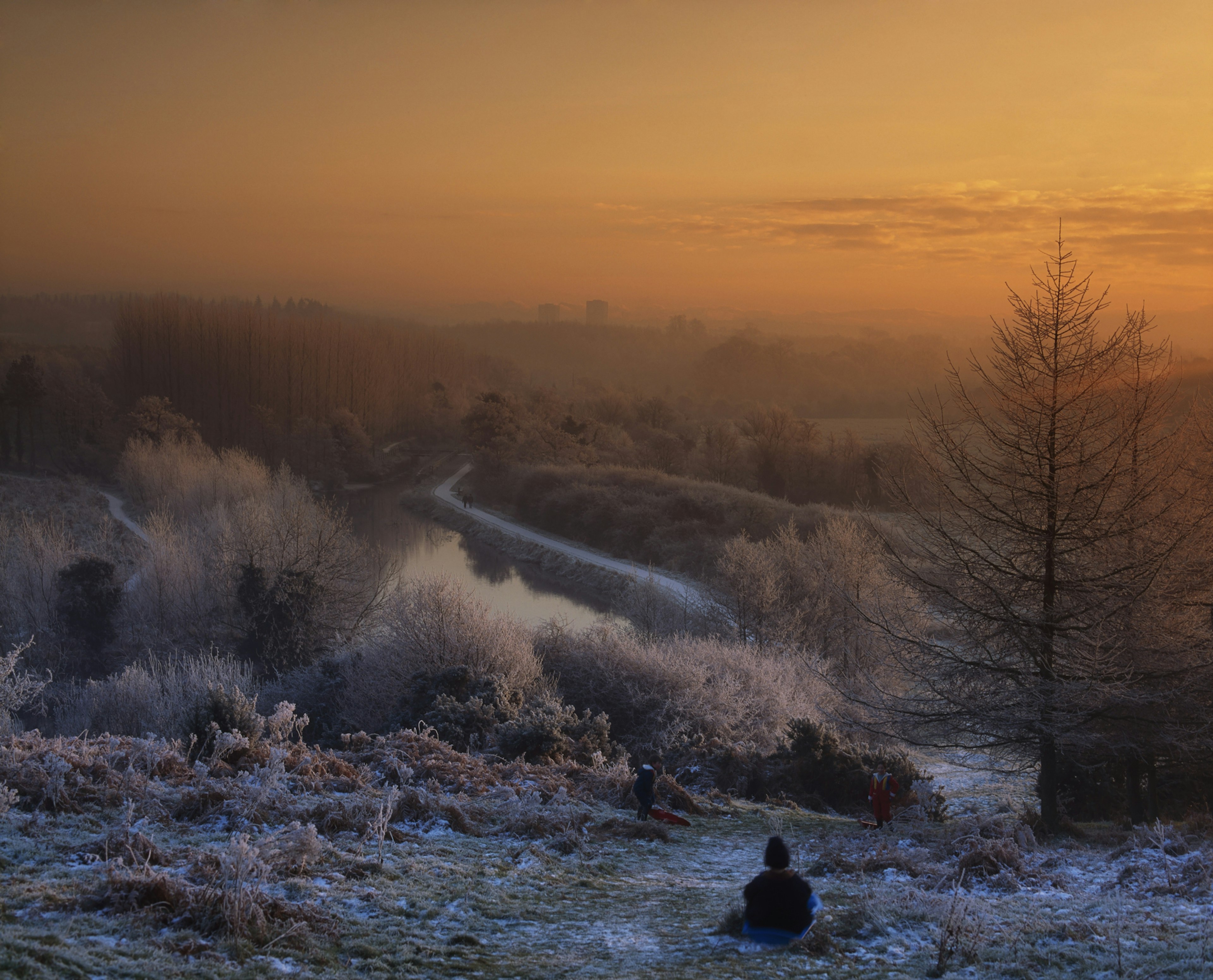 An orange sun sets across the frost-covered hills and trees of Lagan Meadows in Belfast