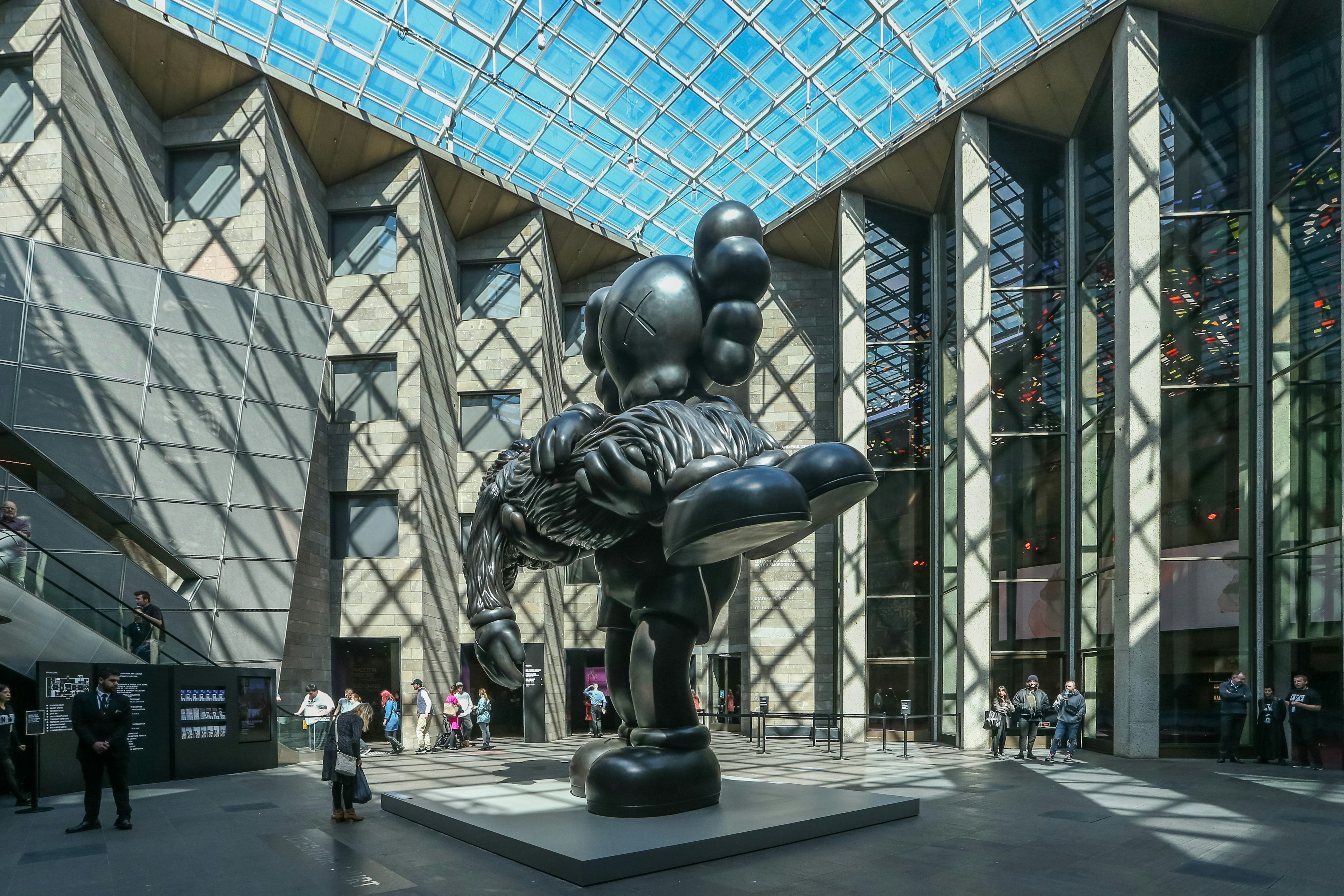 A giant black surrealist statue stands in the centre of a large courtyard with a glass ceiling, part of the National Gallery of Victoria, Melbourne