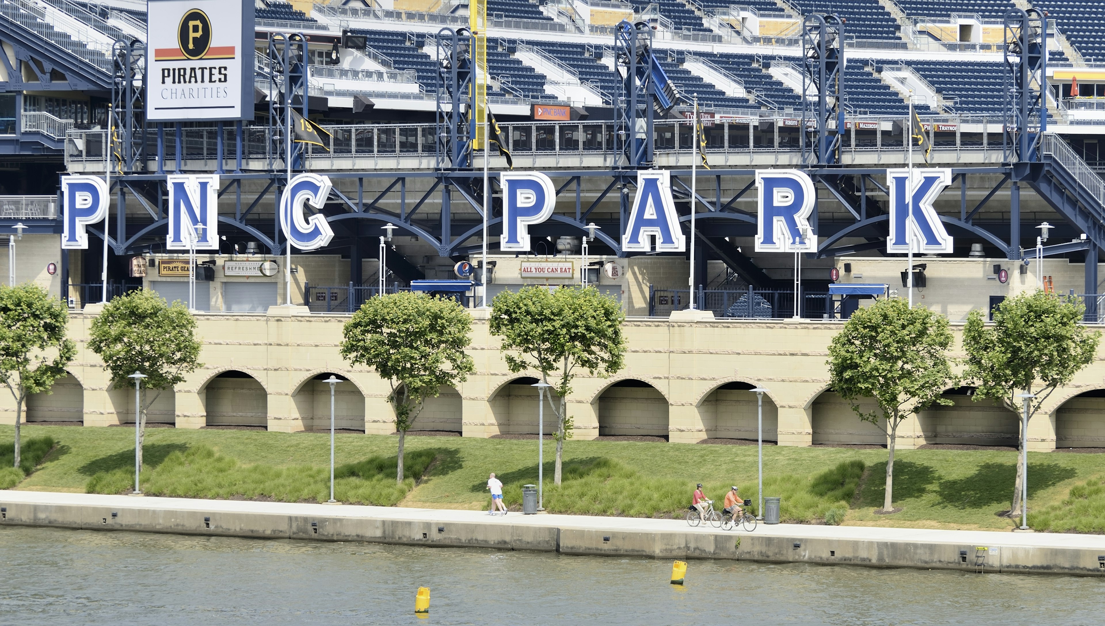 Exterior of PNC Field in Pittsburgh, Pa. There are people riding bikes on a concrete waterfront in front of the stadium.