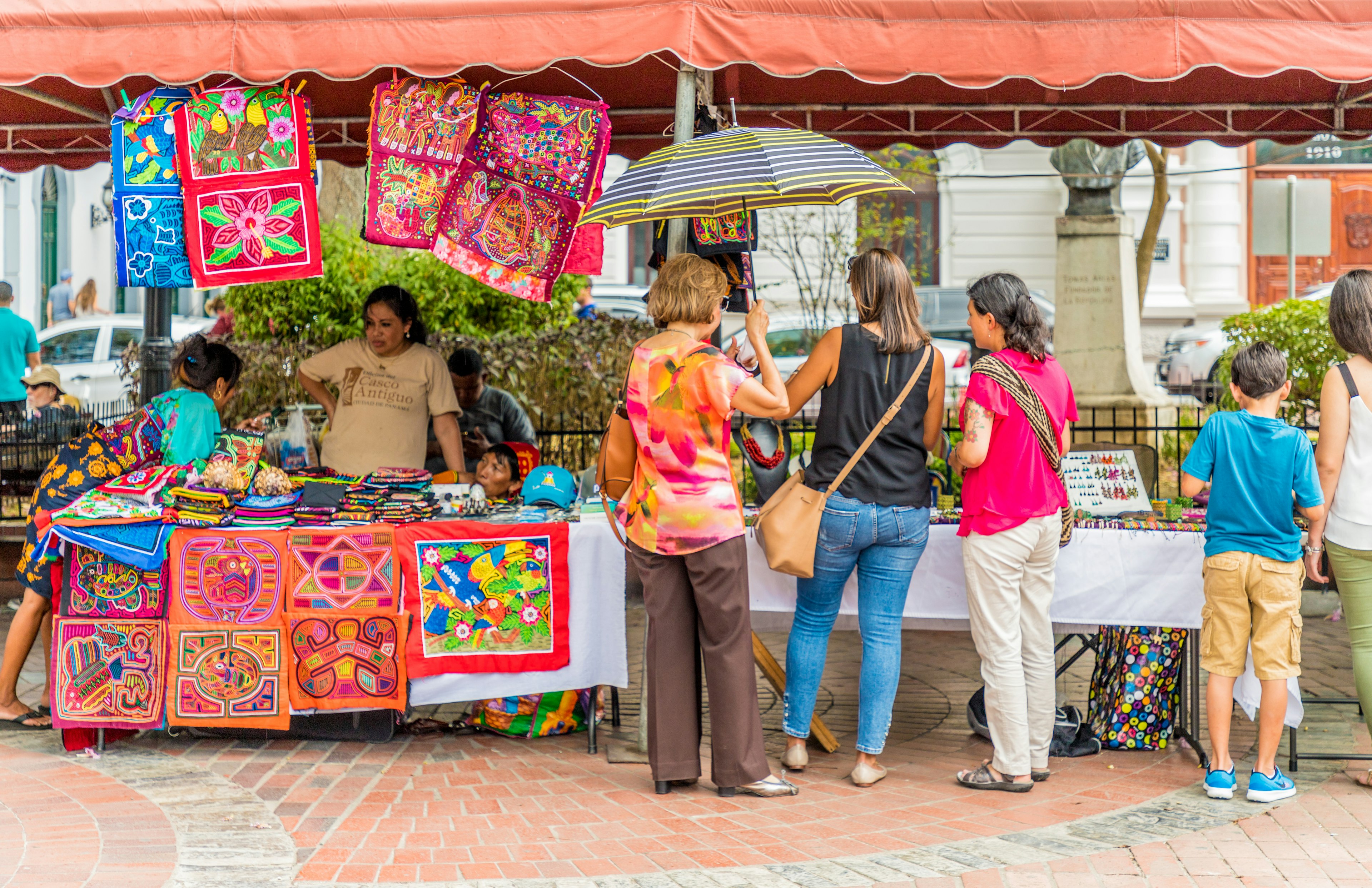 A group of travelers look over tables filled with souvenirs at an outdoor market in Panama City, Panama.