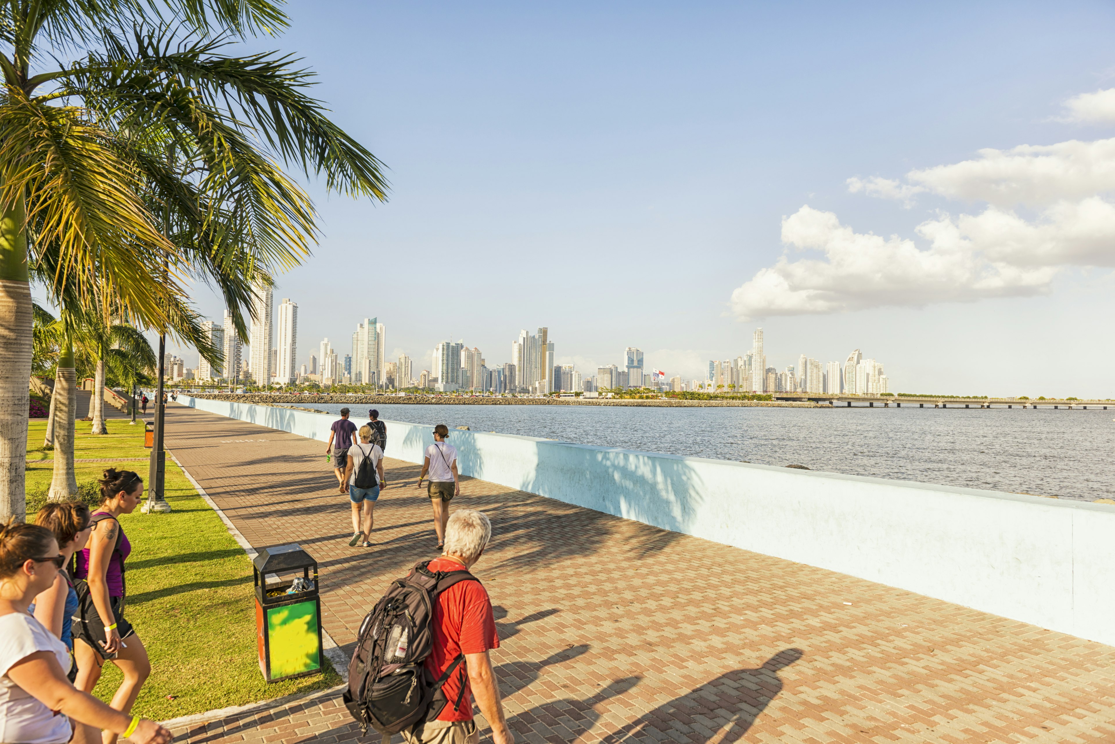 Tourists in Panama city walking along a waterside pathway with the city's skyline in the background