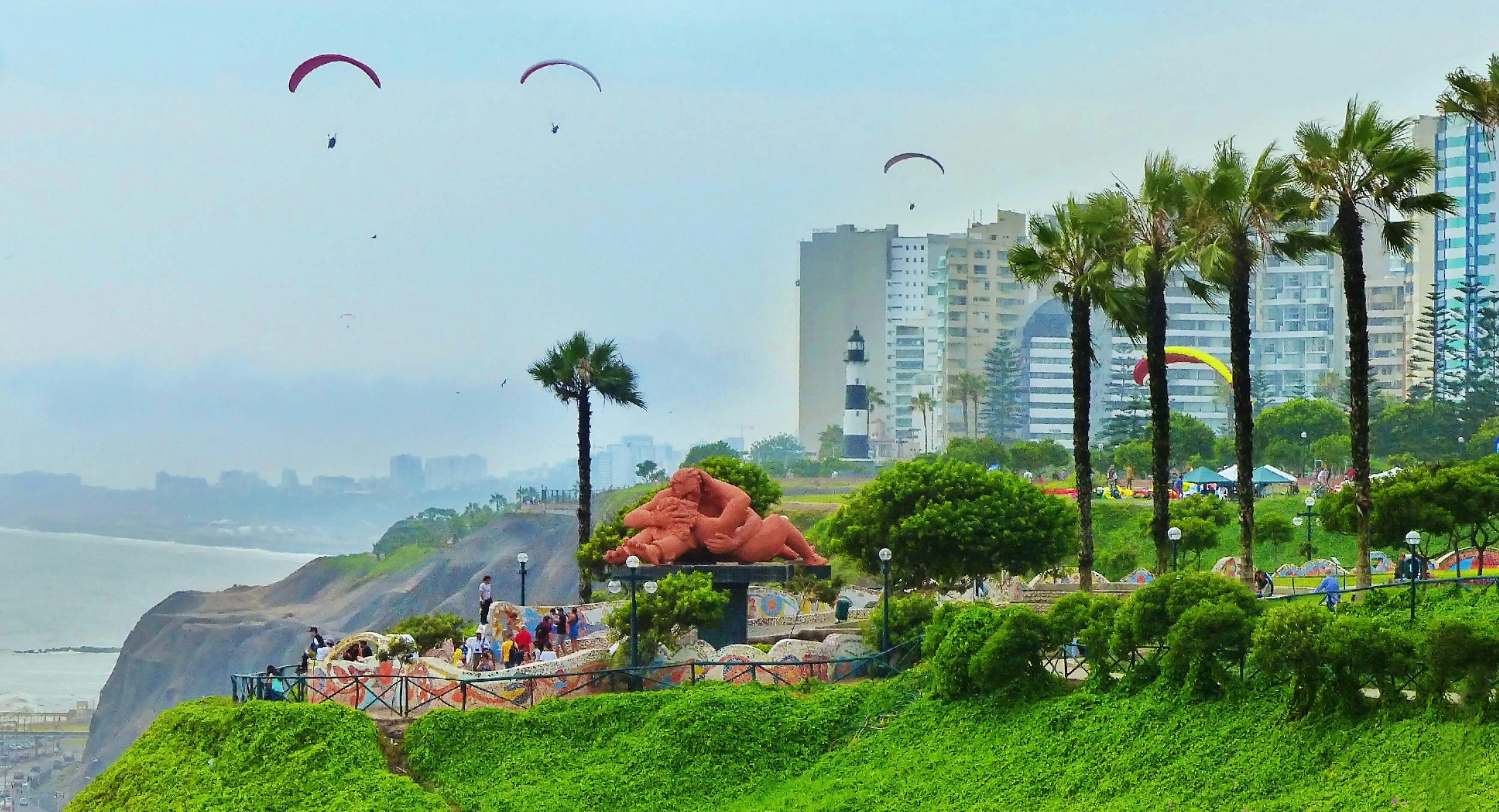 View of paragliders over the Park of Love and tourists mingling by the El Beso sculpture