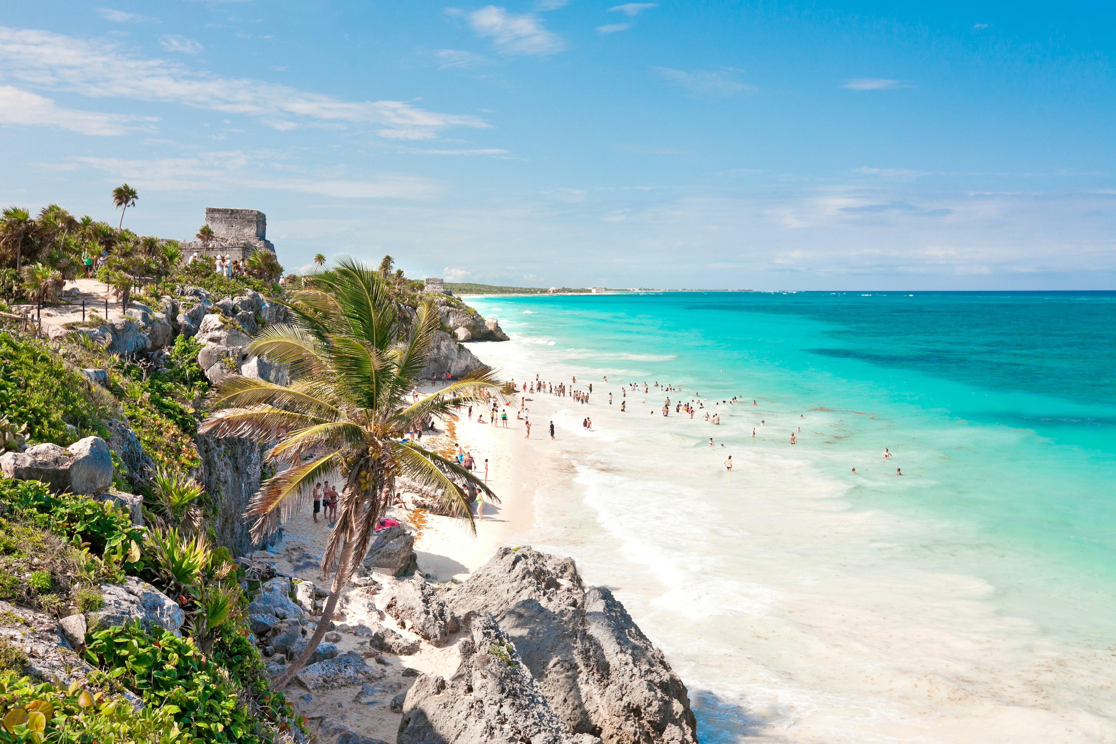 Panoramic view of a white-sand beach with ruins and people in the distance