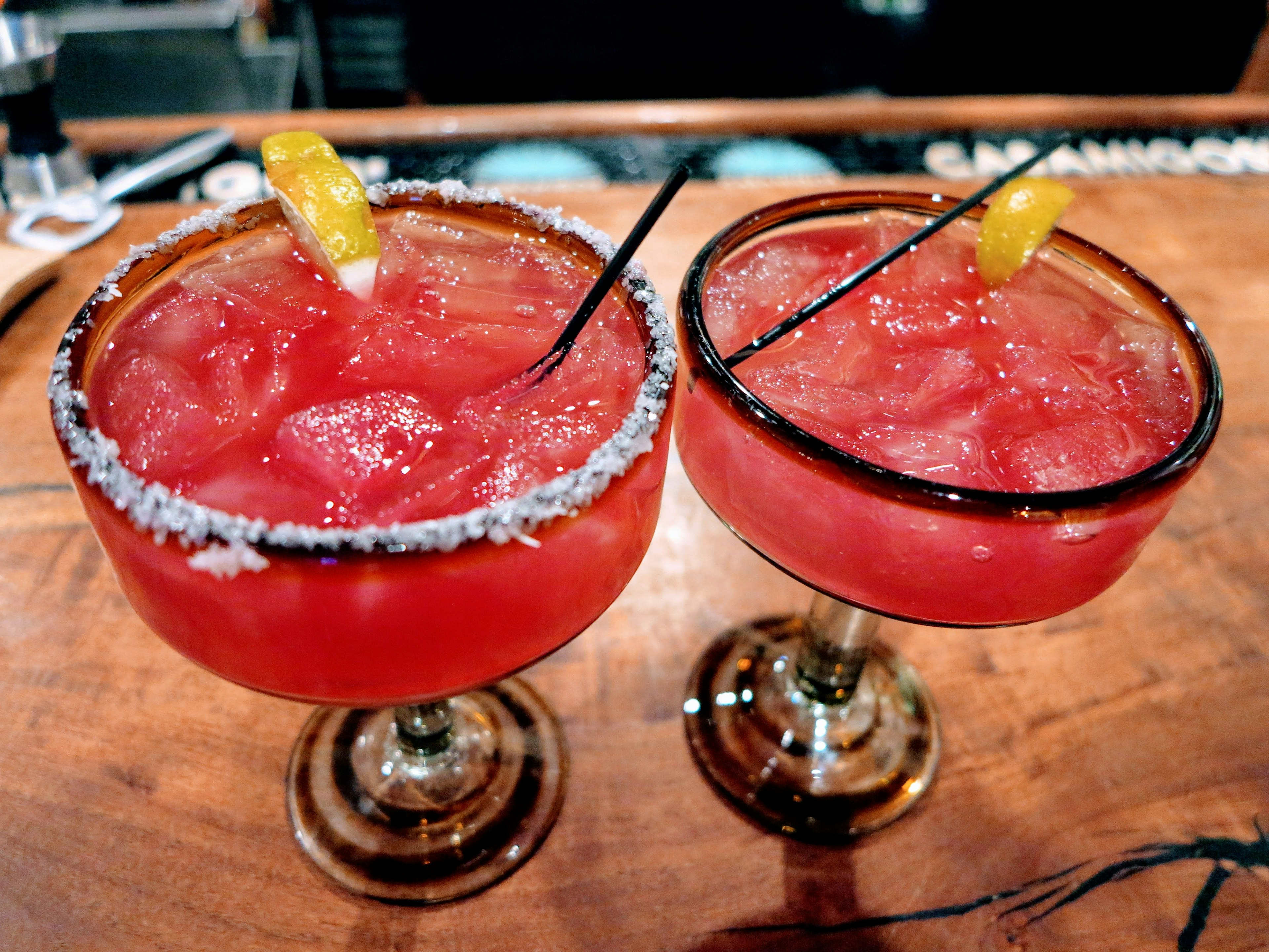 A pair of Prickly Pear Margaritas in glasses on a bar. One is rimmed with salt.