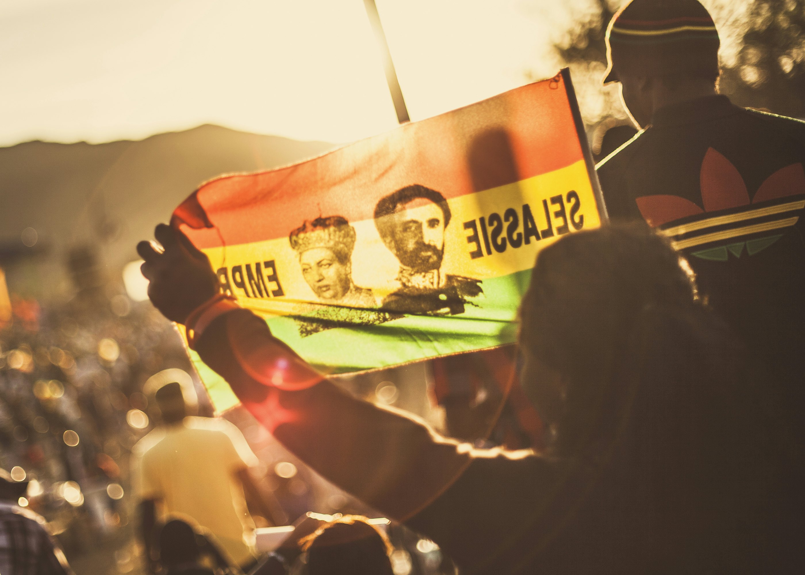 A woman waves a flag with a picture of Haile Selassie against sunrise while watching Capleton perform at the Rebel Salute Festival