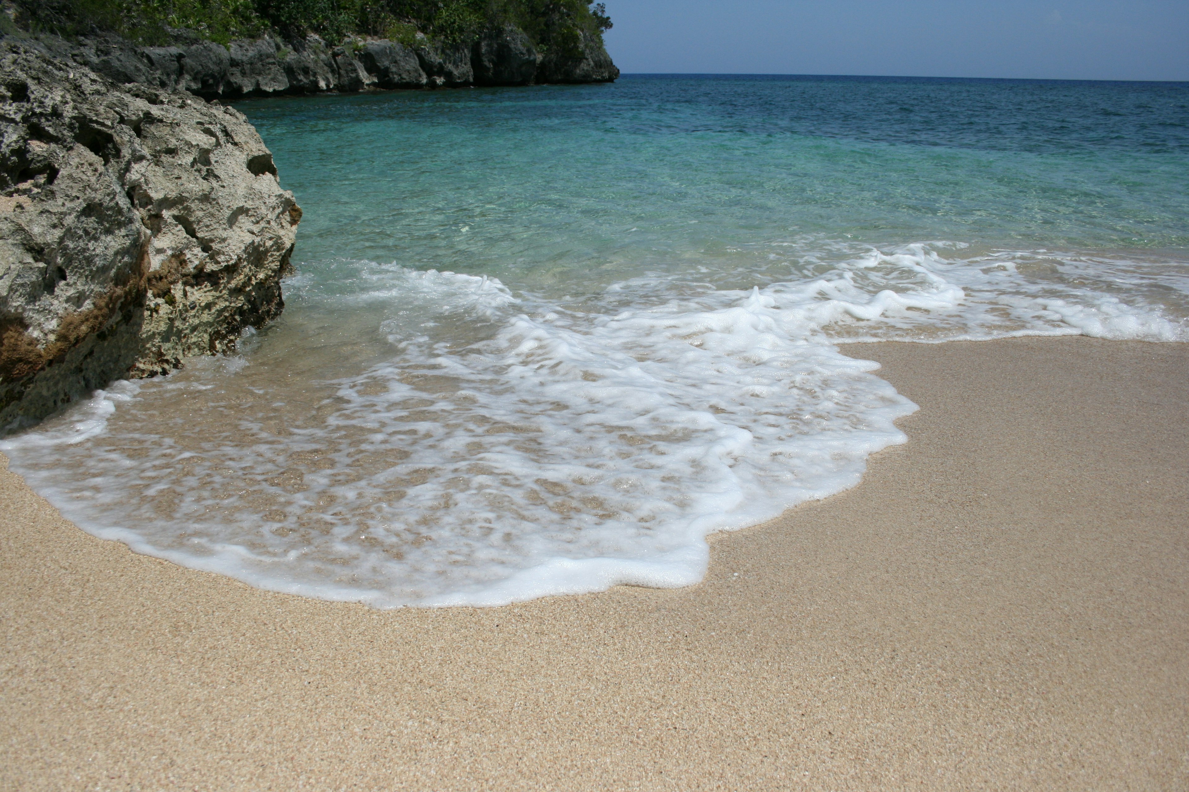 Gentle waves lap on the shore next a large rock jutting into the sea.