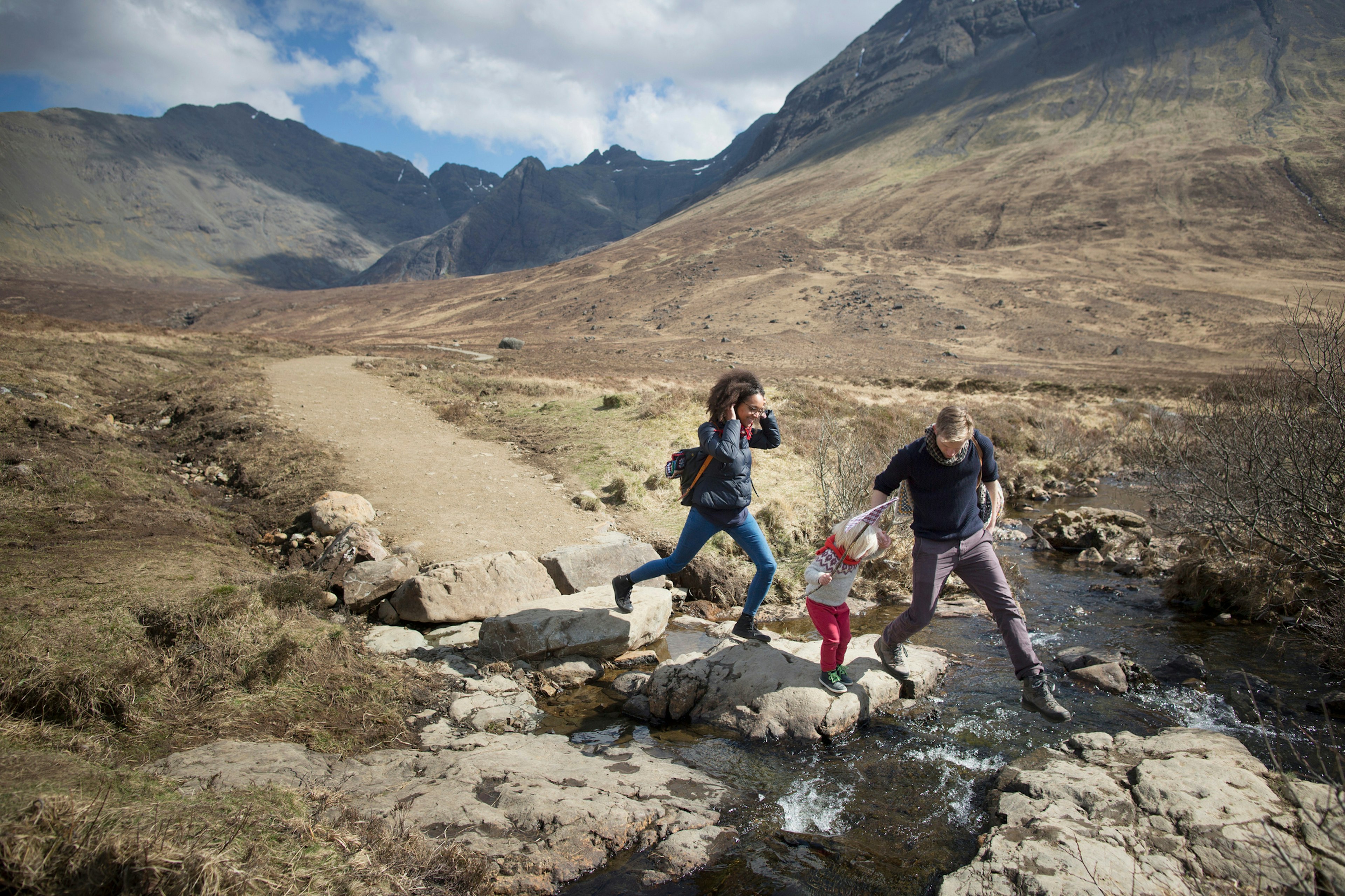 A family with a young toddler follow a hiking trail and cross a stream