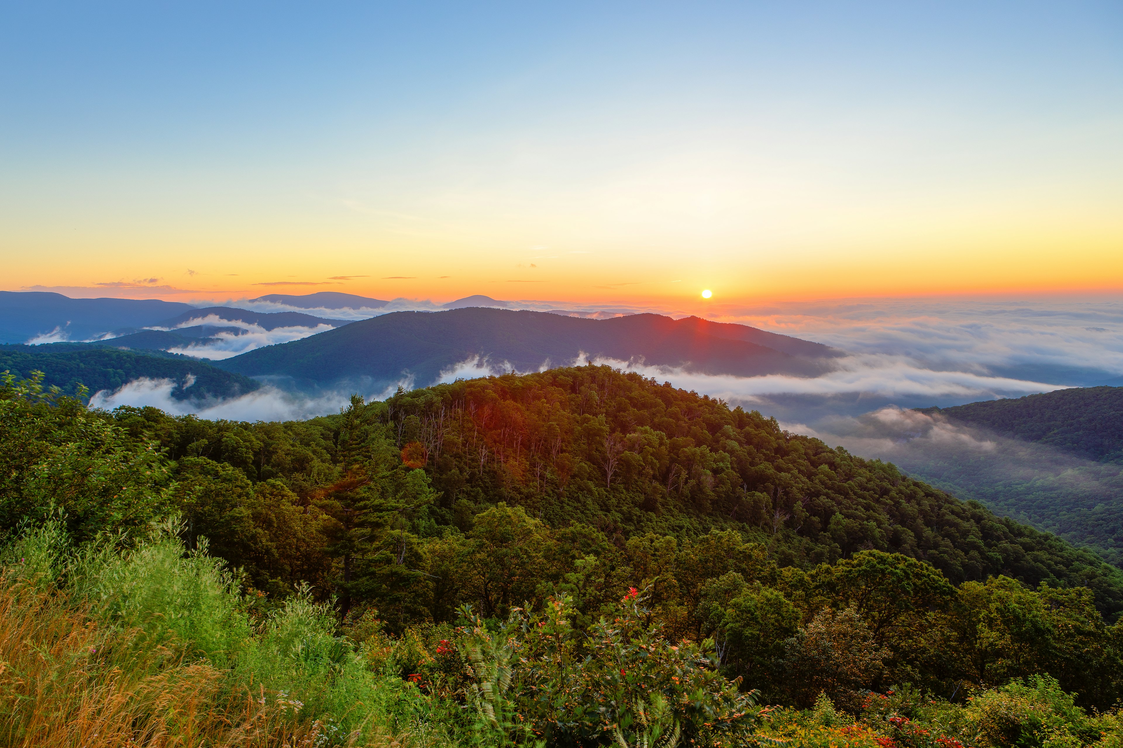 The sun rises over vast hilly landscape, with some cloud covering the valleys below