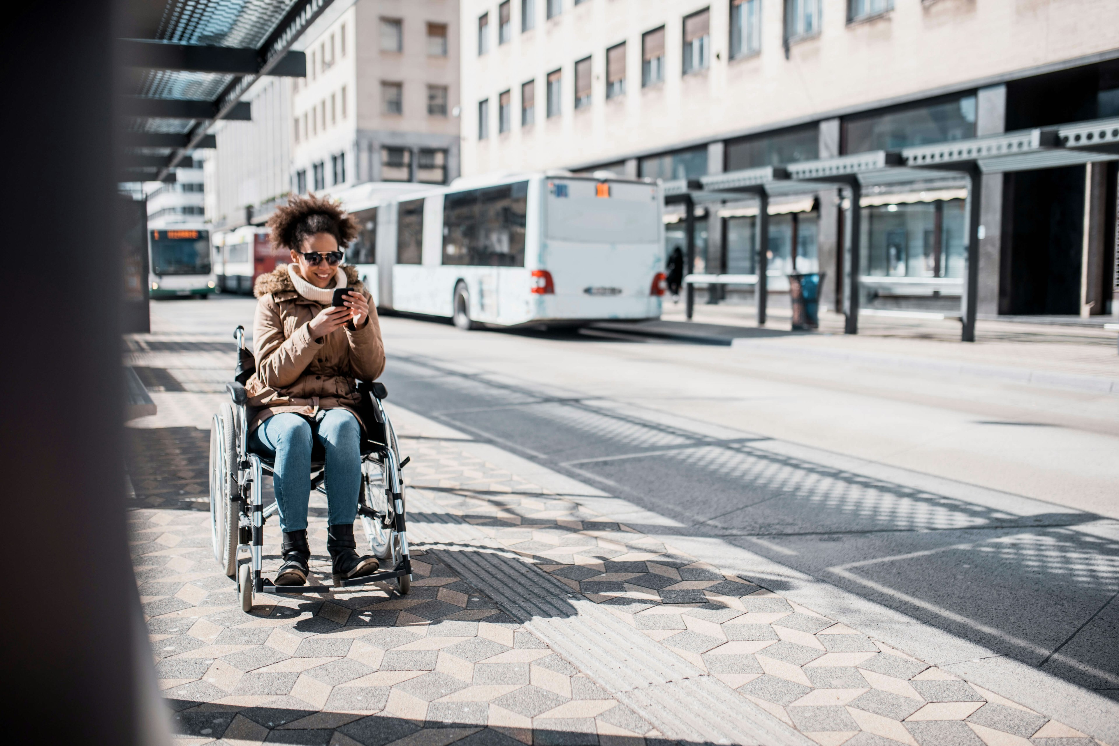 A woman in wheelchair using smart phone and waiting for a bus