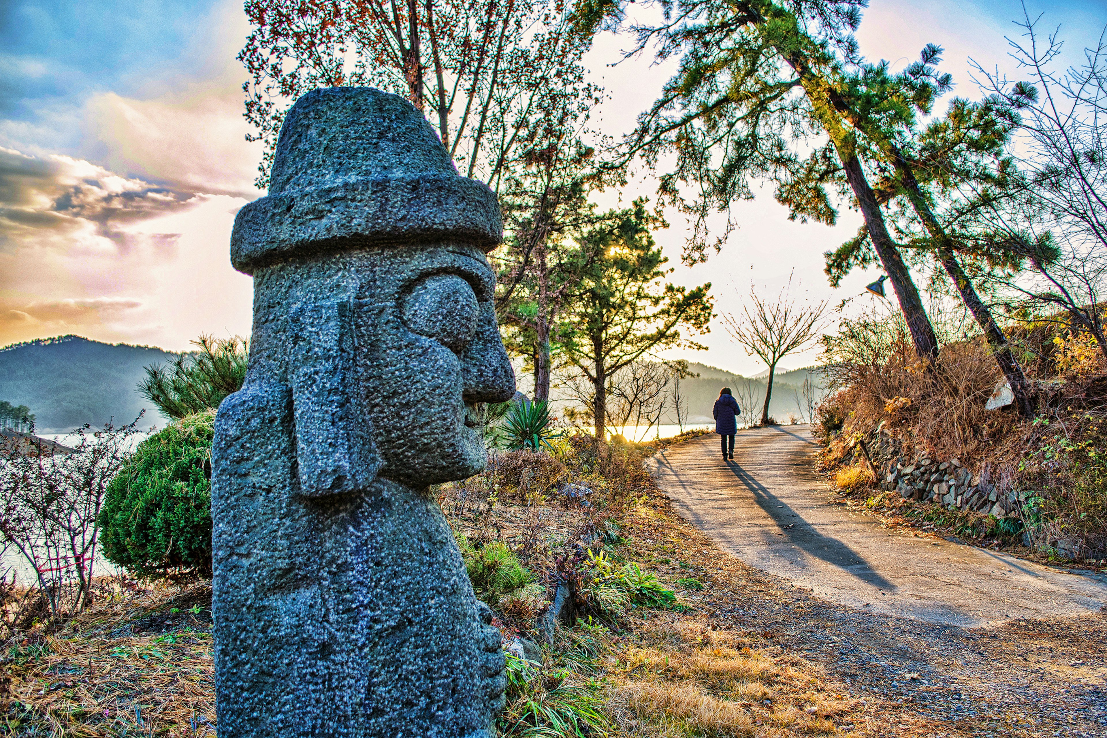 A walker passing a stone statue on Jeju island