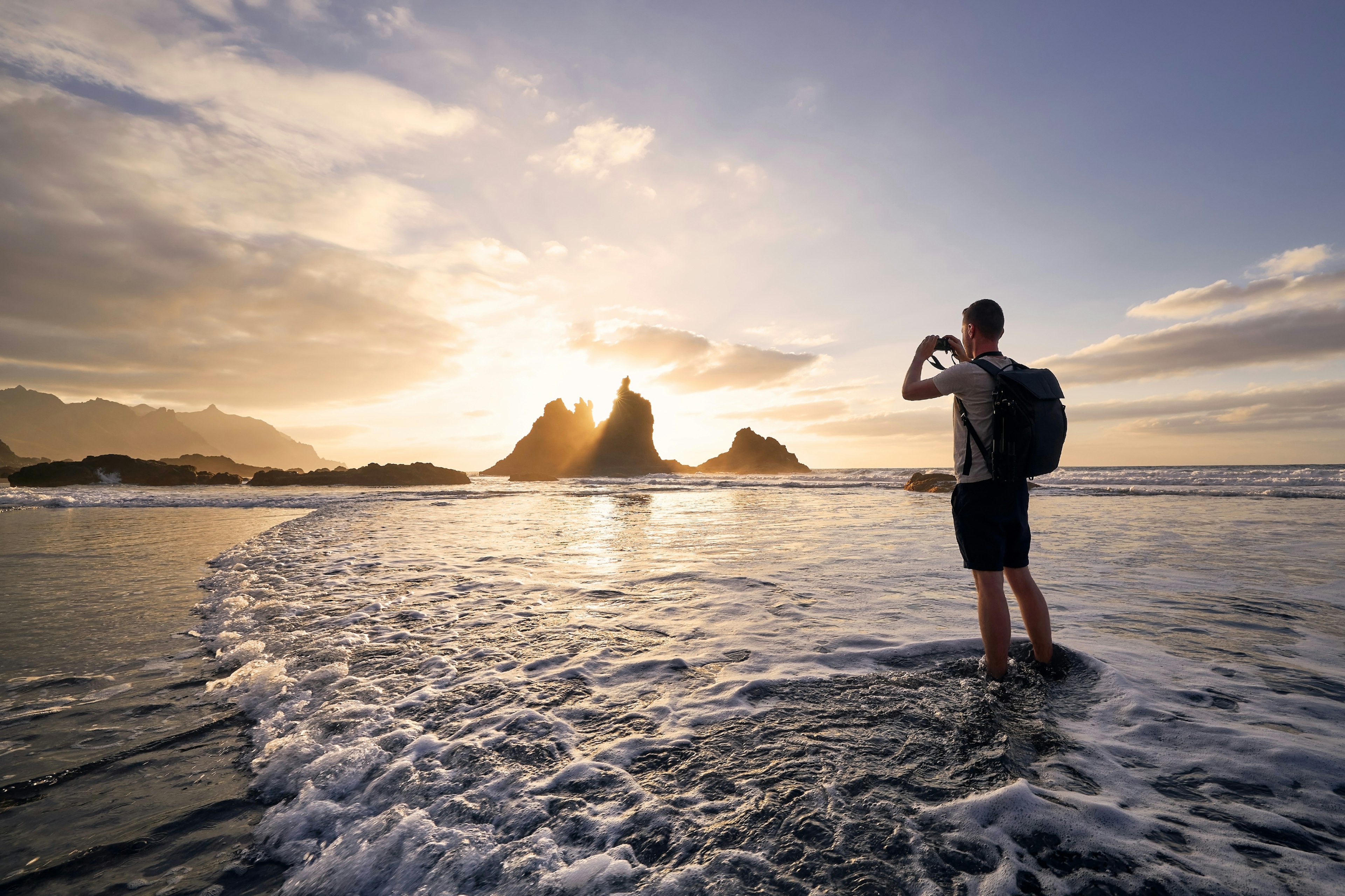 A man is silhouetted against the sunset as he takes a photograph of a spiky rock formation on the coastline in Tenerife