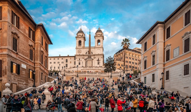 Crowds of people walking up and down the Spanish Steps in Rome, with a two-spired church at the top of the steps