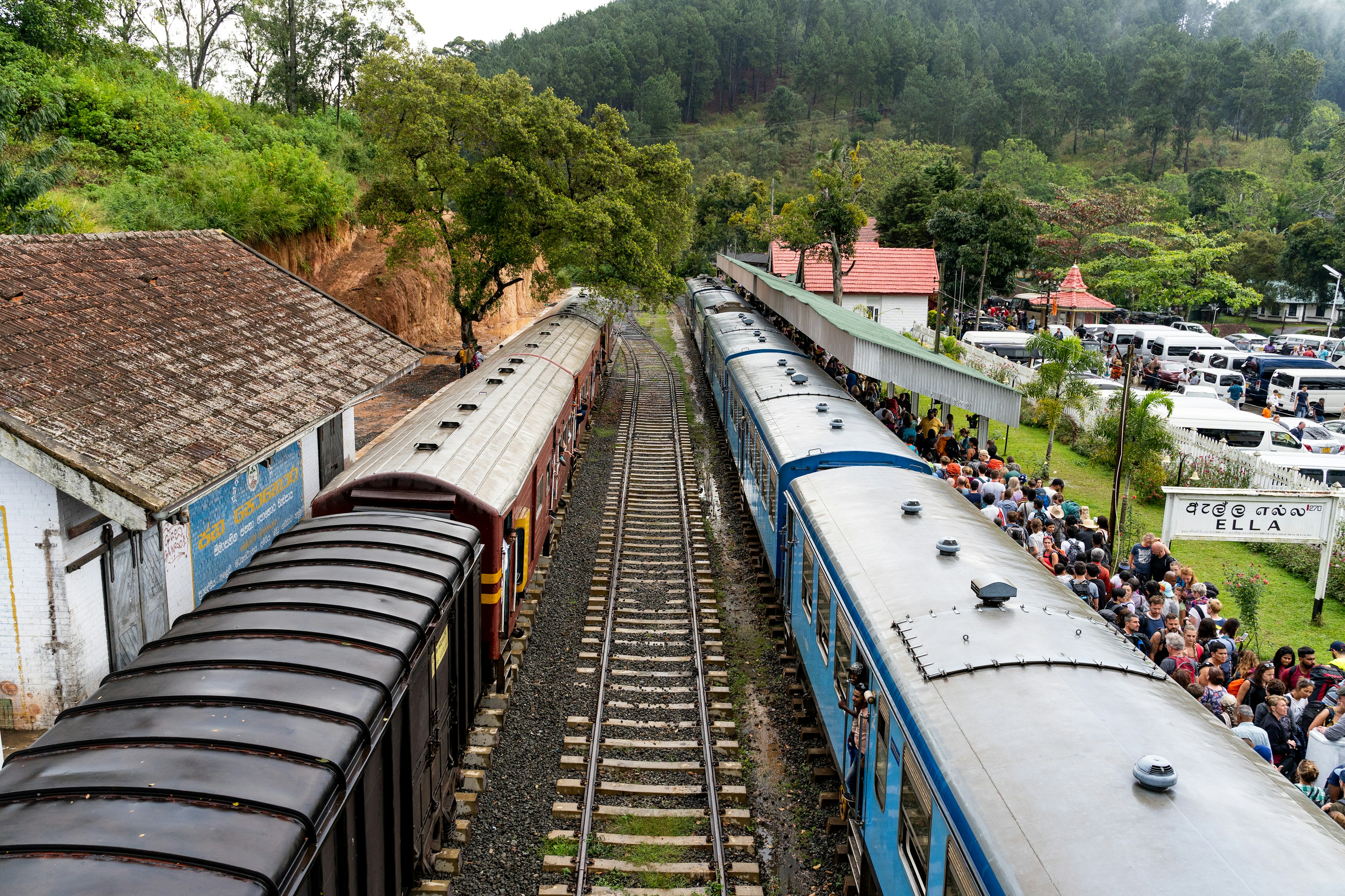 An aerial shot of two trains at a station. The right-hand platform is packed with people