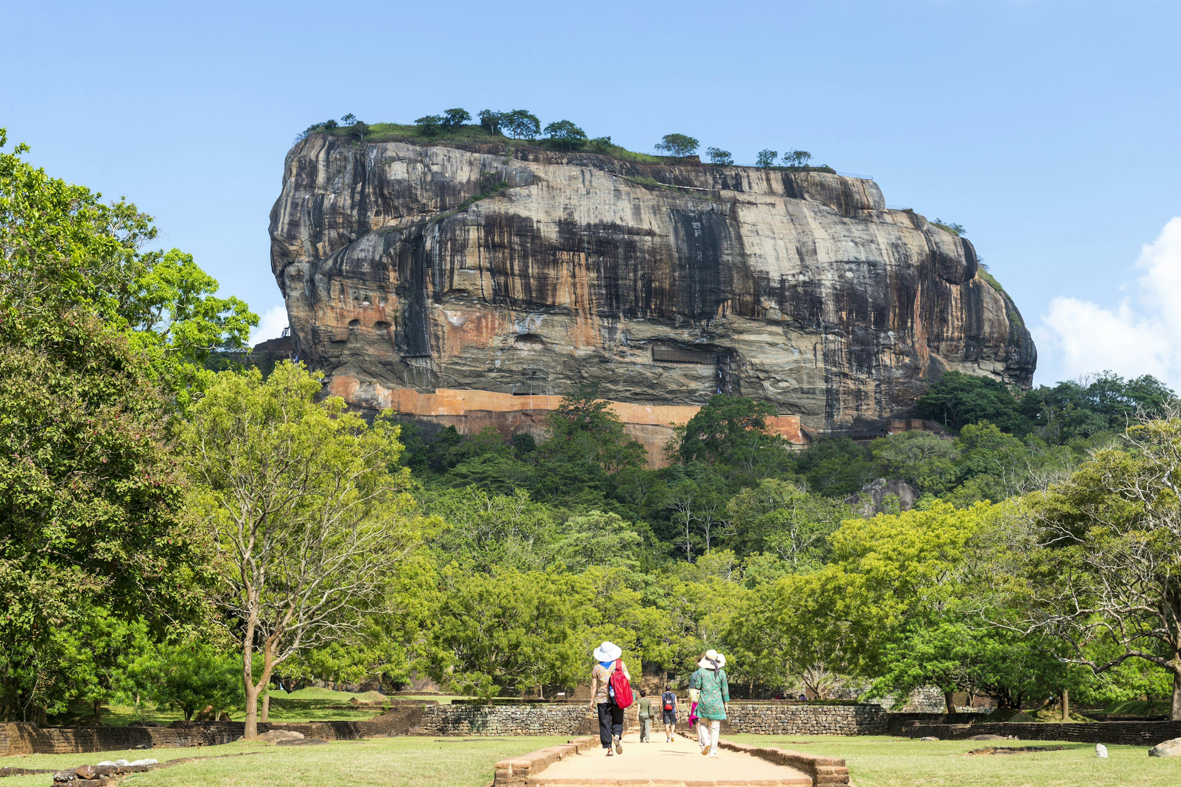 People follow a path approaching a huge rocky outcrop, perfect for climbing