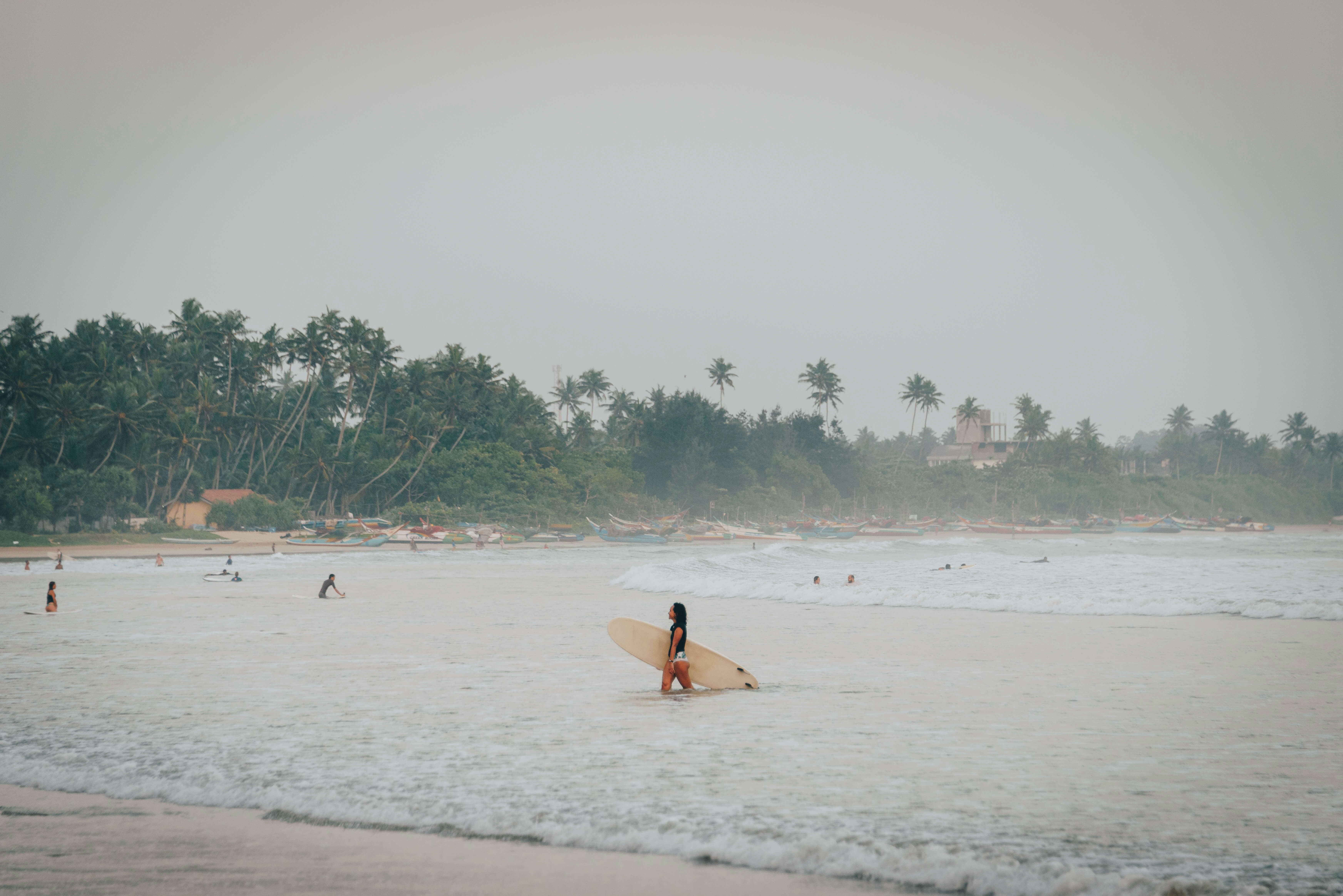 Surfers in the water at beach in Sri Lanka on a hazy, rainy day.