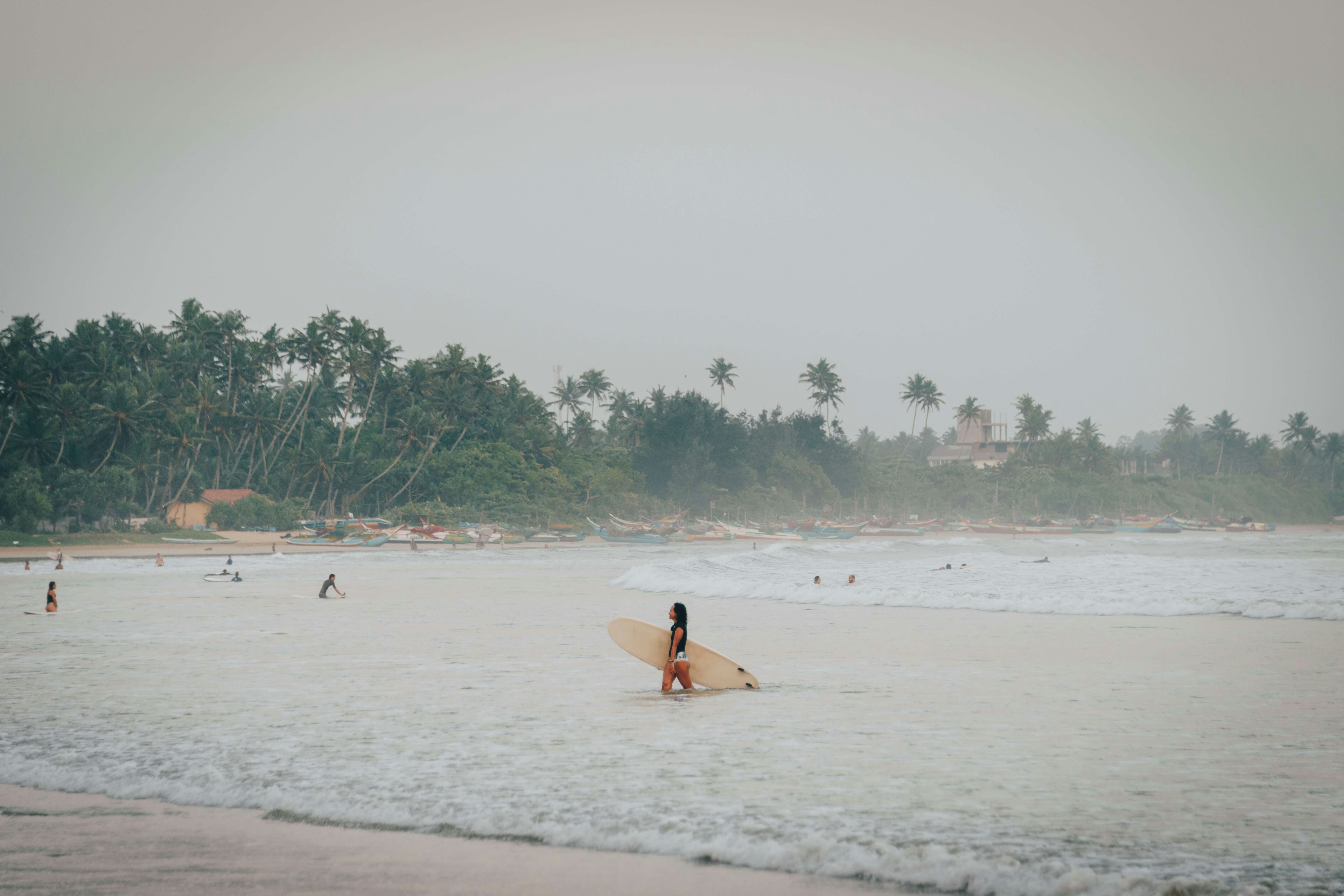 Surfers at Weligama beach in Sri Lanka on a hazy, rainy day